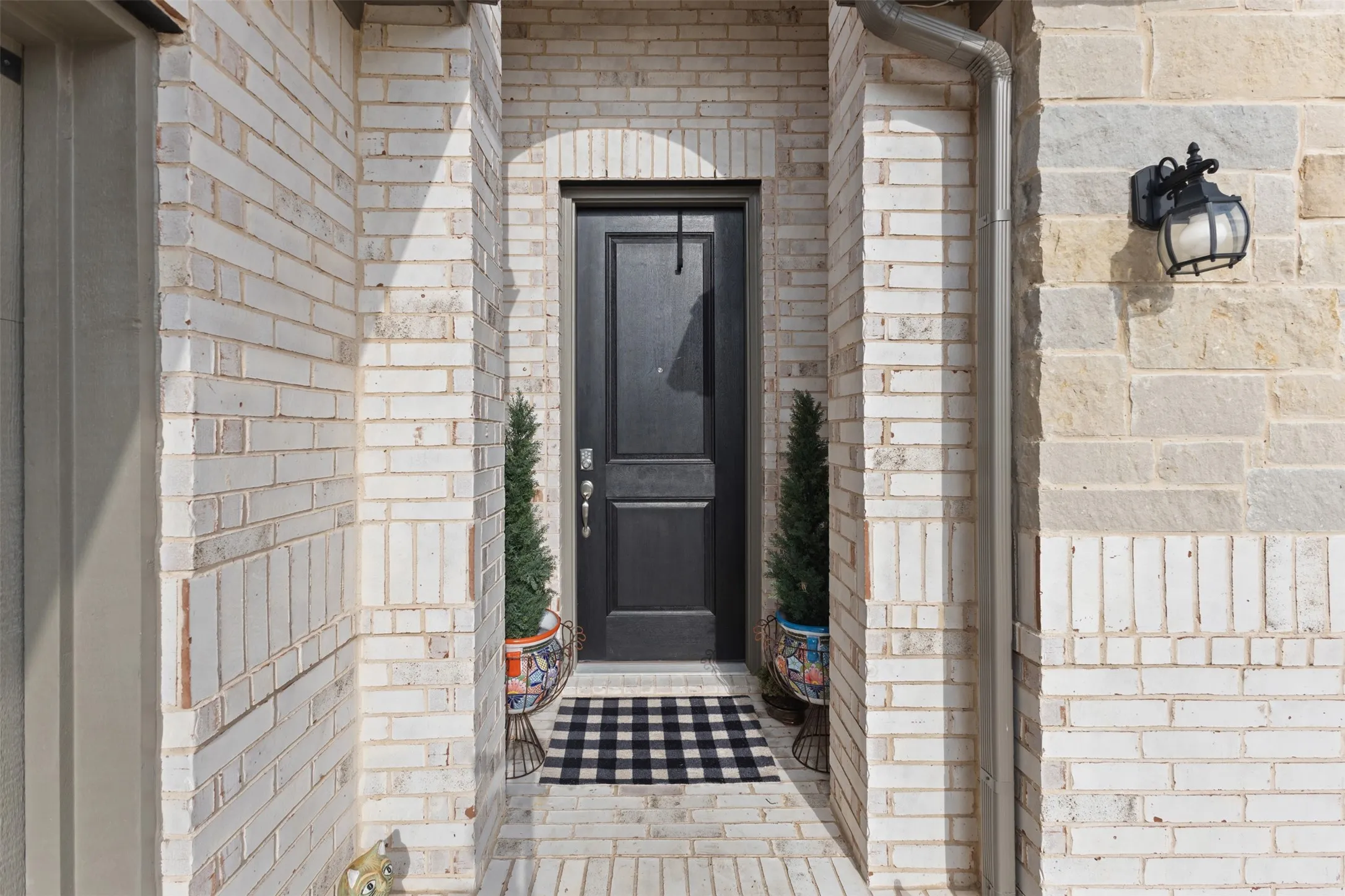 Front entry with a dark-paneled door, arched brickwork, light-toned brick facade, contrasting stone accents, and a classic-style exterior light fixture