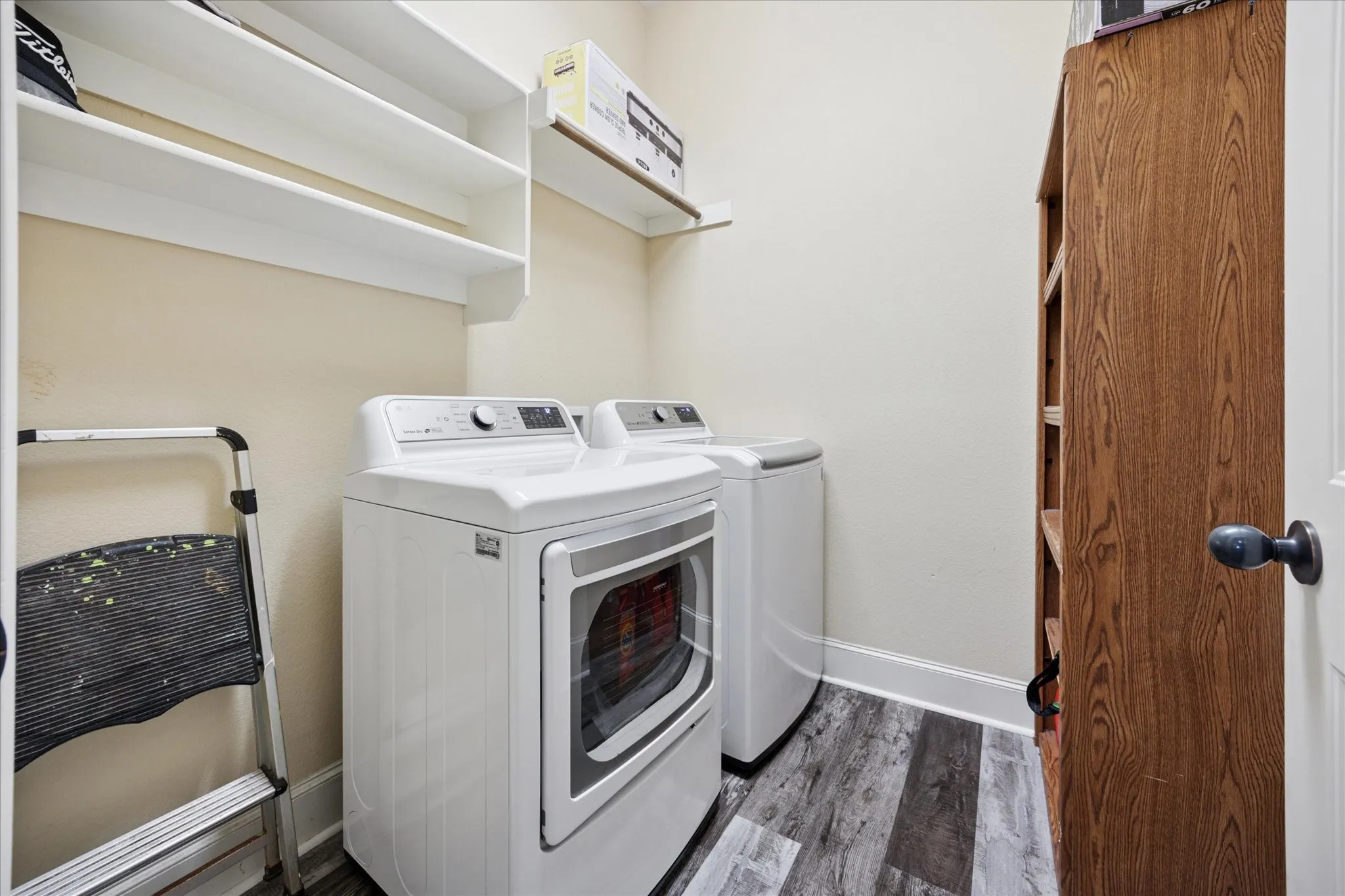 Laundry area featuring white built-in shelving, wood-finish flooring, and a stand-alone wood-finish storage unit