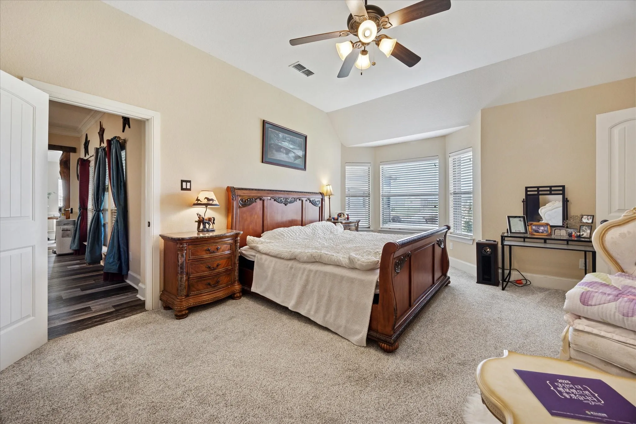 Spacious room featuring carpet flooring, a vaulted ceiling with a ceiling fan, and a bay window configuration
