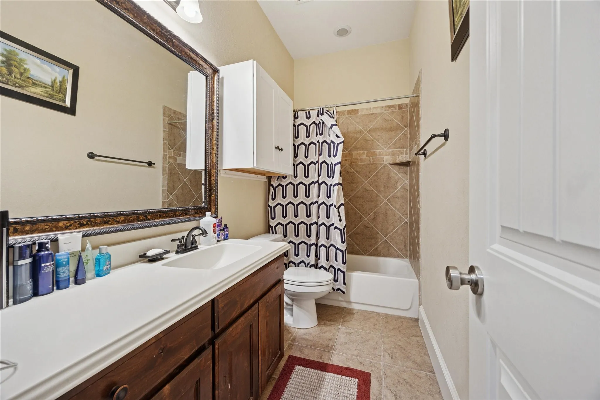 Bathroom featuring a wood-finish vanity with an integrated sink, a large framed mirror, and a shower-over-tub combination with tile surround