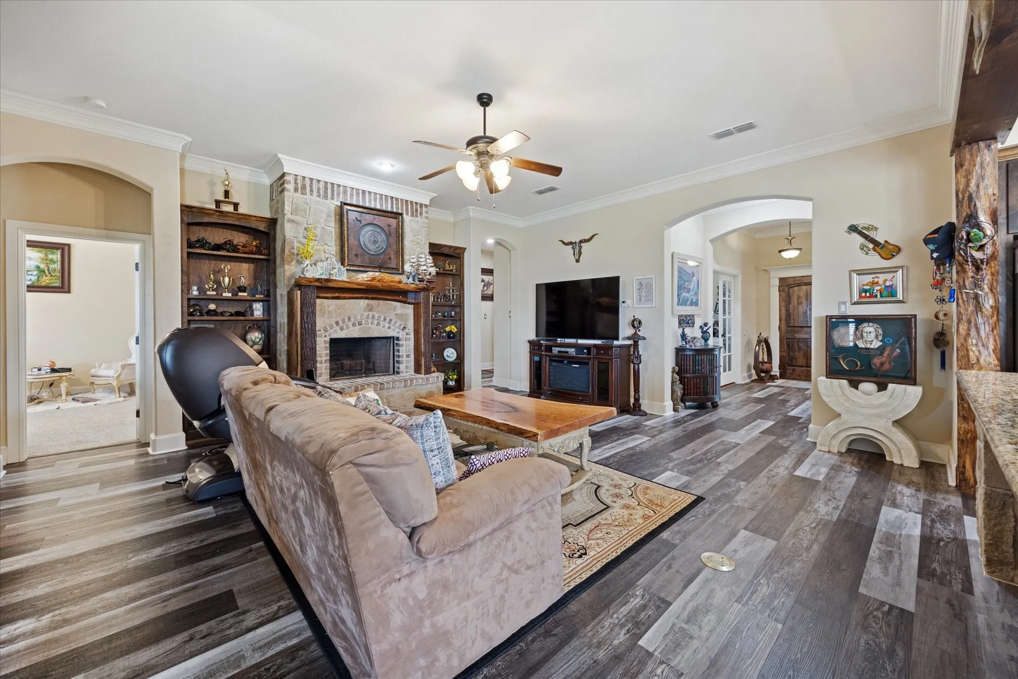 Living area featuring wood-finish flooring, a stone and brick fireplace with an ornate wooden mantel, crown molding, and built-in shelving