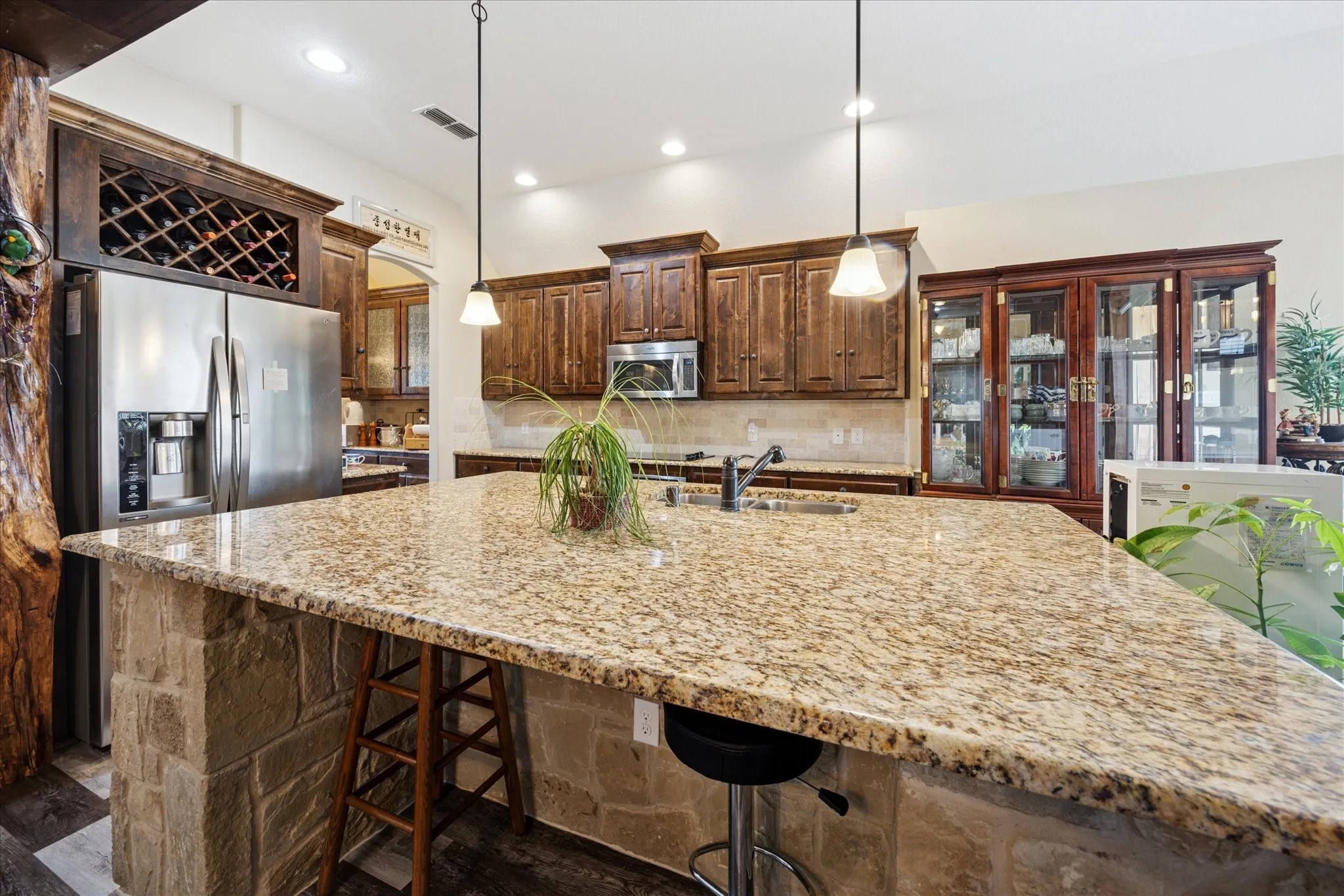 Kitchen featuring a large stone-wrapped island with a granite countertop, stainless steel appliances, dark wood cabinetry, and recessed lighting