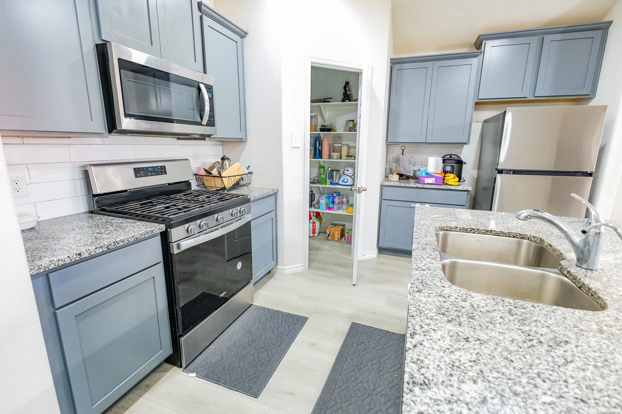 Kitchen featuring light blue cabinetry, stainless steel appliances, speckled countertops, white subway tile backsplash, and light wood-finish flooring