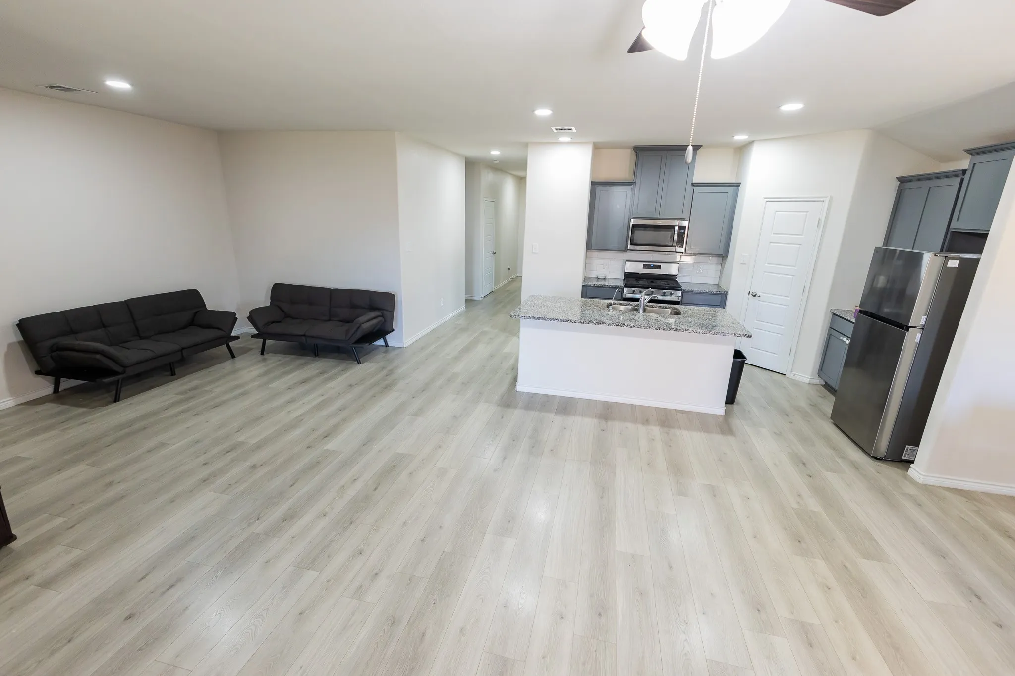 Open-concept living area with wood-finish flooring, recessed lighting, a ceiling fan, a kitchen island with stone countertops, and stainless steel appliances