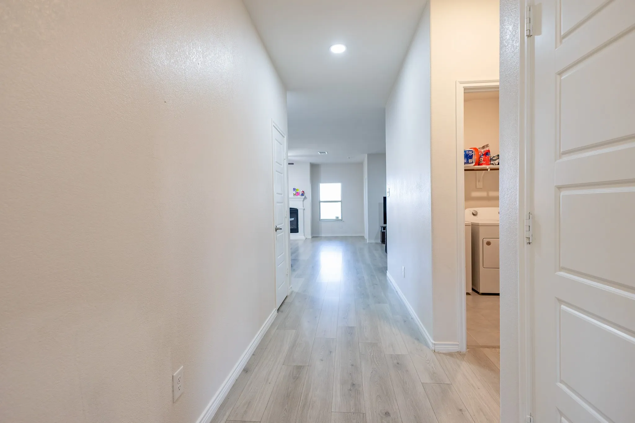 Hallway with light wood-finish flooring extending into living spaces