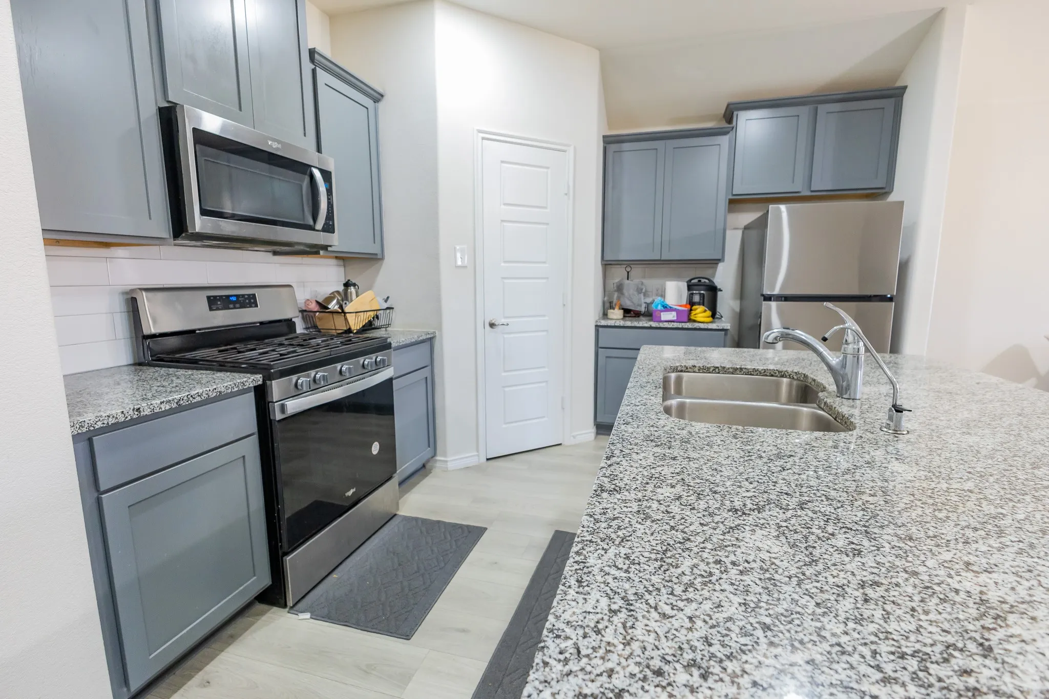 Contemporary kitchen featuring light gray cabinetry, stainless steel appliances, speckled stone countertops, a white subway tile backsplash, and light wood-finish flooring