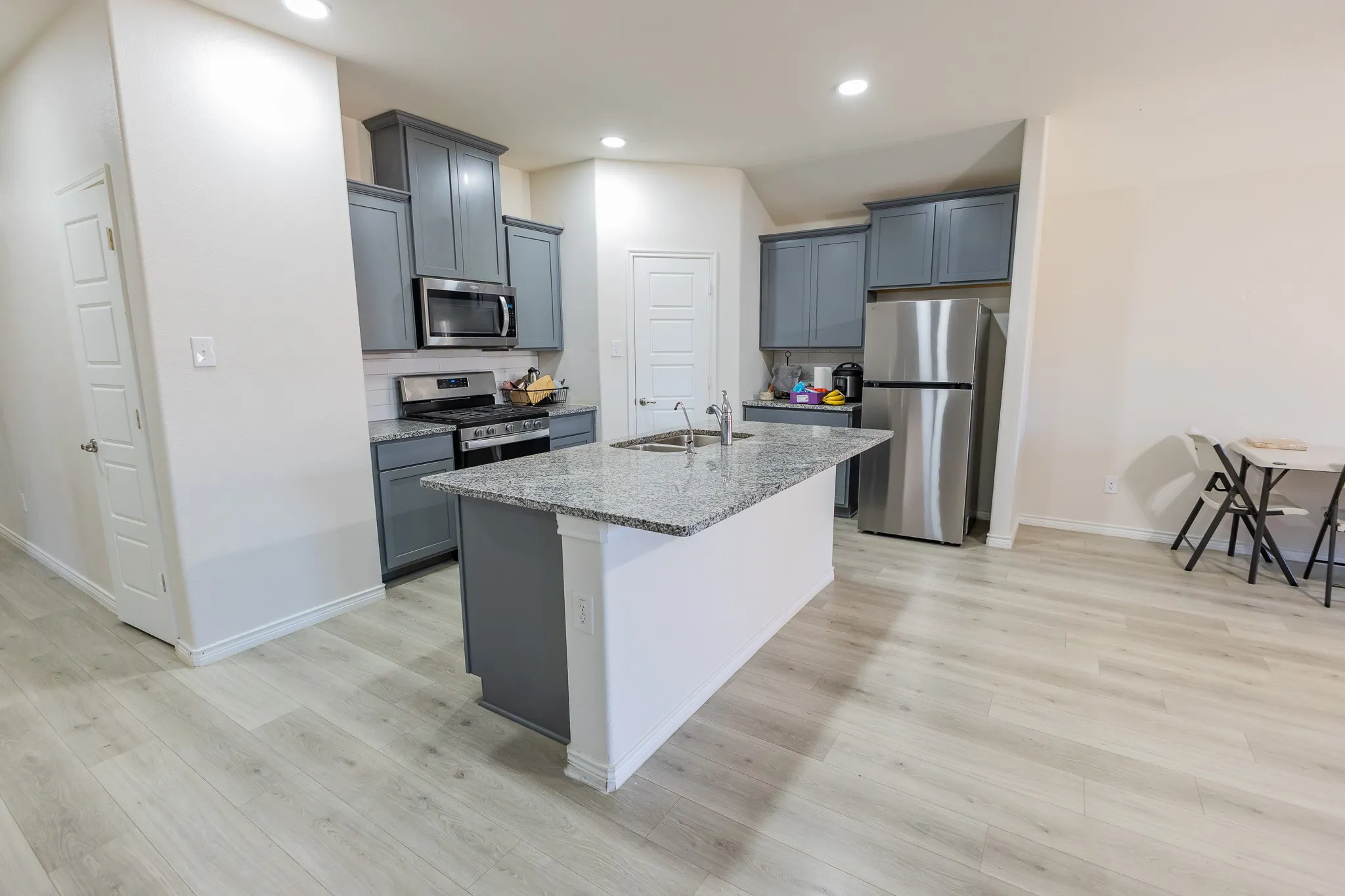 Open concept kitchen featuring an island with a light-toned countertop, gray cabinetry, stainless steel appliances, and wood-finish flooring