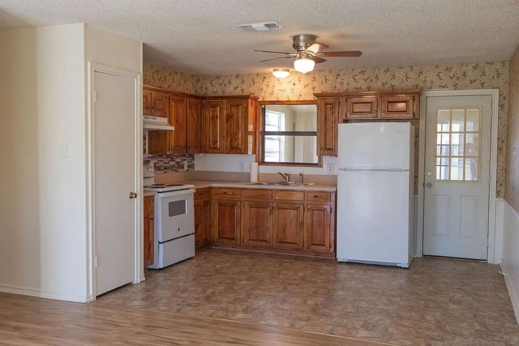 Kitchen featuring wood-finish cabinetry, tile backsplash, laminate countertops, and a full suite of white appliances