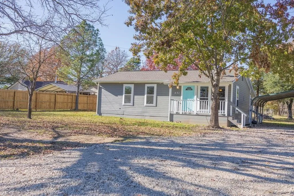 Gray exterior featuring a turquoise front door, white porch railing, and a gravel driveway