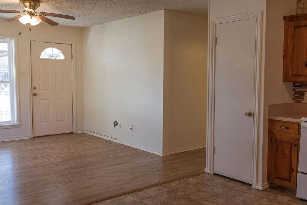 Interior space featuring wood-finish flooring, a white paneled entry door with an arched window, and a ceiling fan with light fixture