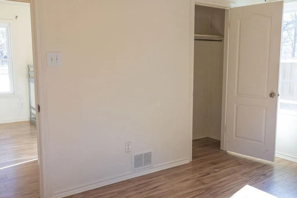Room featuring wood-finish flooring, light-toned wall paint, and a built-in closet with a panel door and interior hanging rod