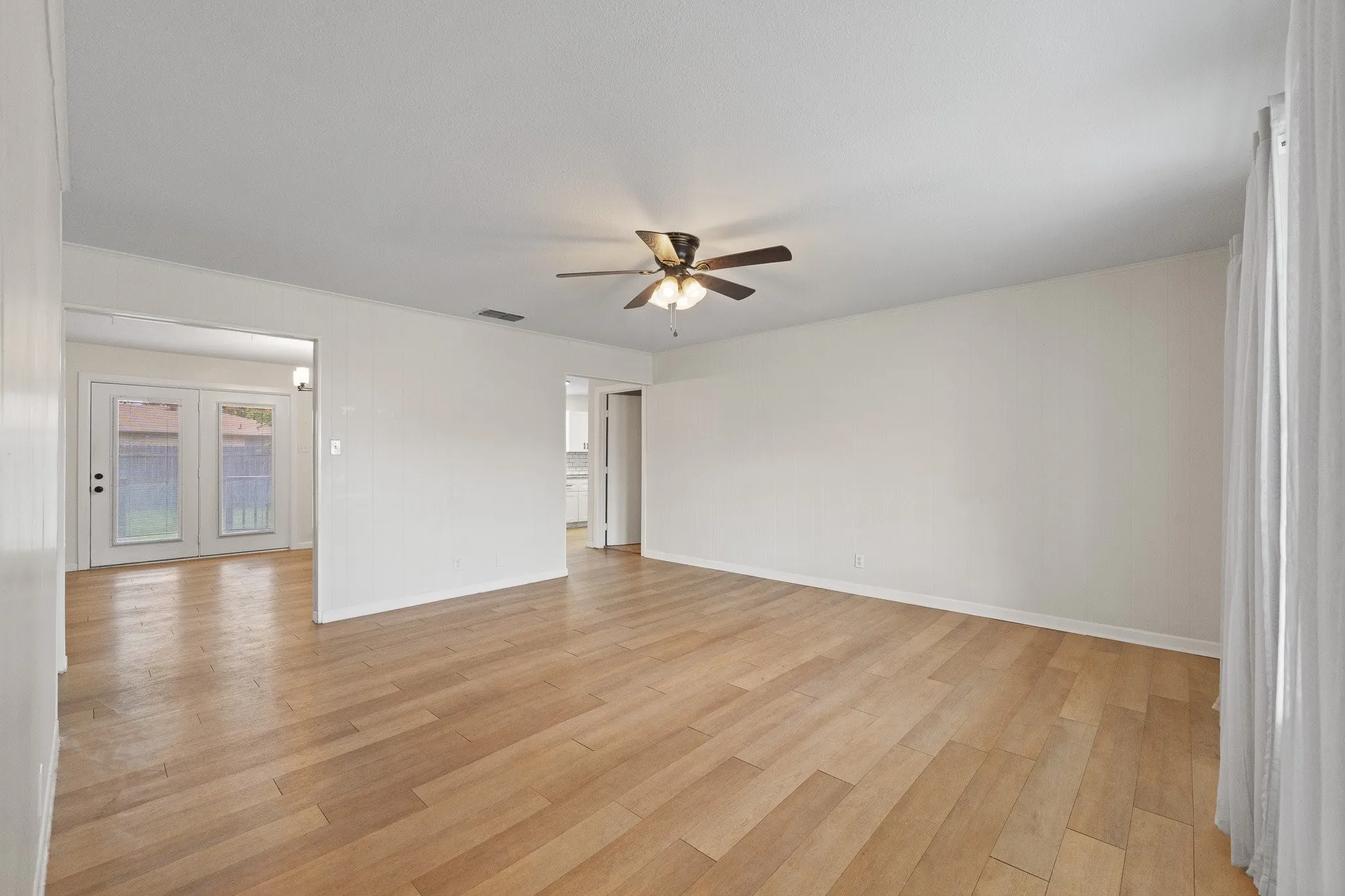 Expansive interior space featuring wood-finish flooring, a ceiling fan with integrated lighting, and multiple entryways