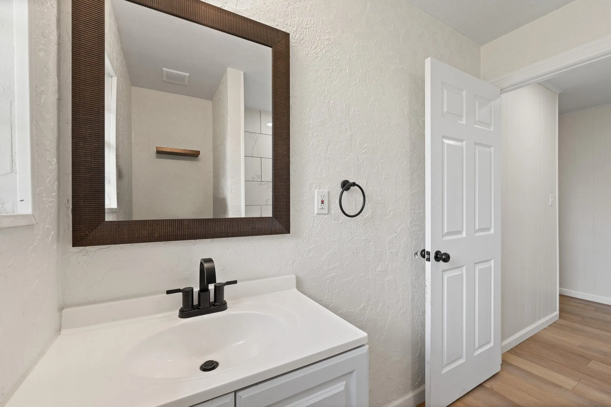Bathroom vanity featuring a white countertop with an integrated sink, matte black faucet, and a large framed mirror