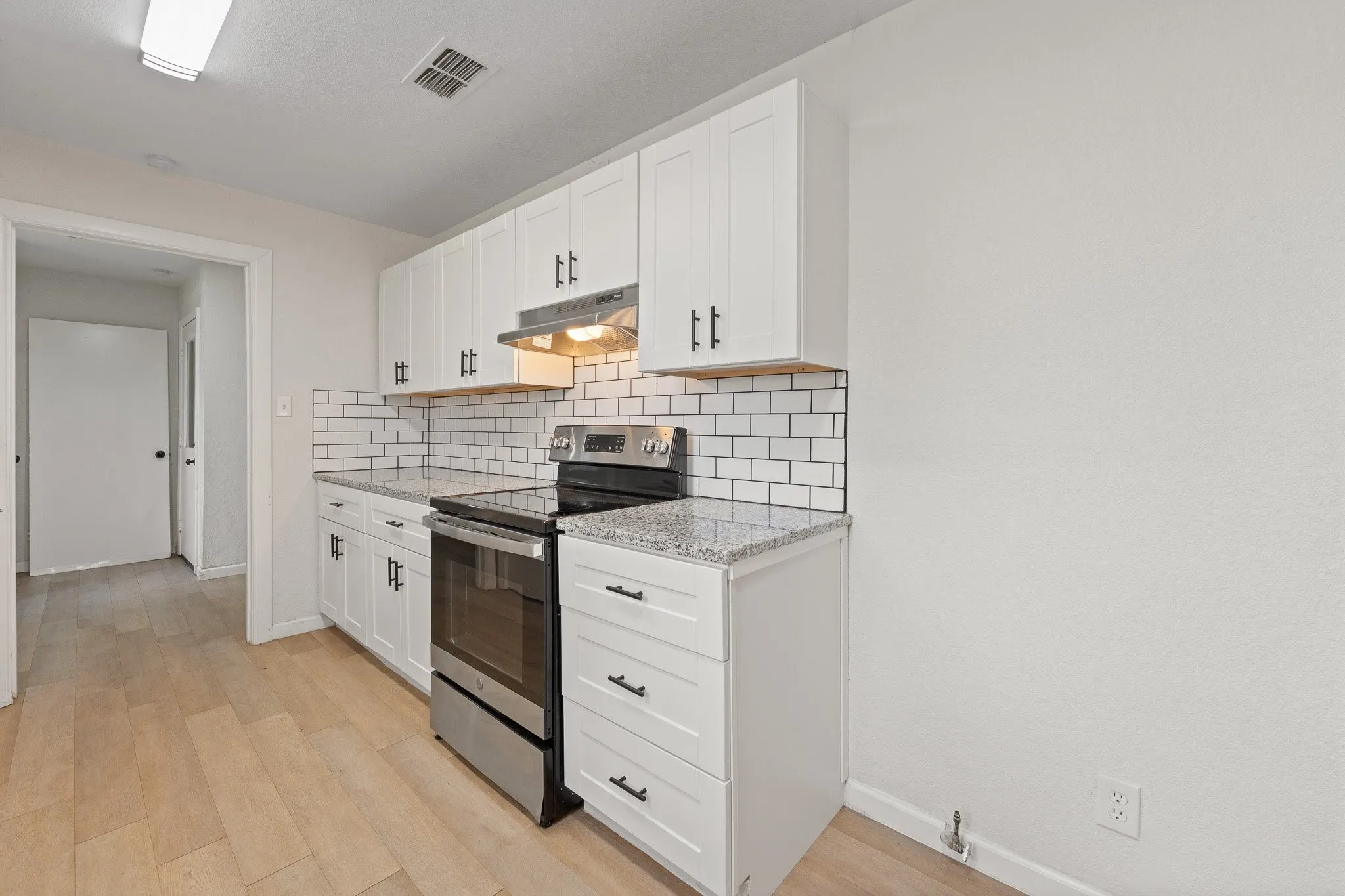Modern kitchen featuring white shaker cabinets, light wood-finish flooring, stainless steel appliances, granite countertops, and a white subway tile backsplash