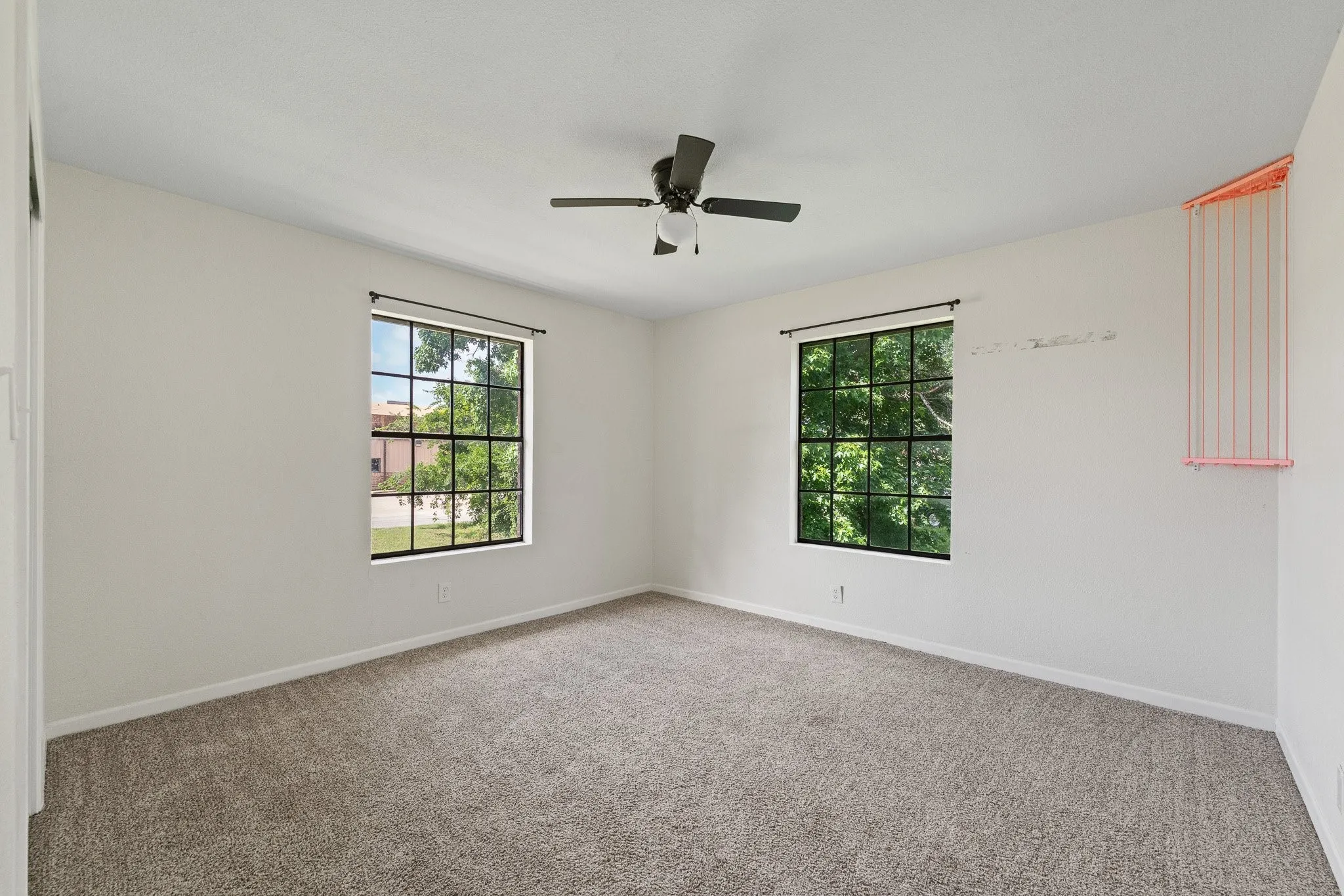 Carpeted room featuring two grid-paned windows, a ceiling fan with light fixture, and white wall finishes
