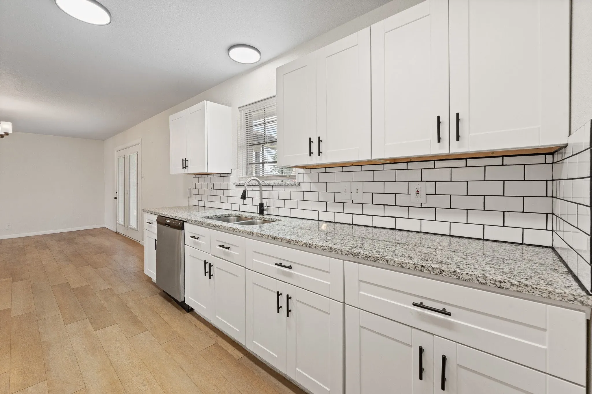 Kitchen with white shaker cabinetry, granite countertops, subway tile backsplash, and stainless steel dishwasher