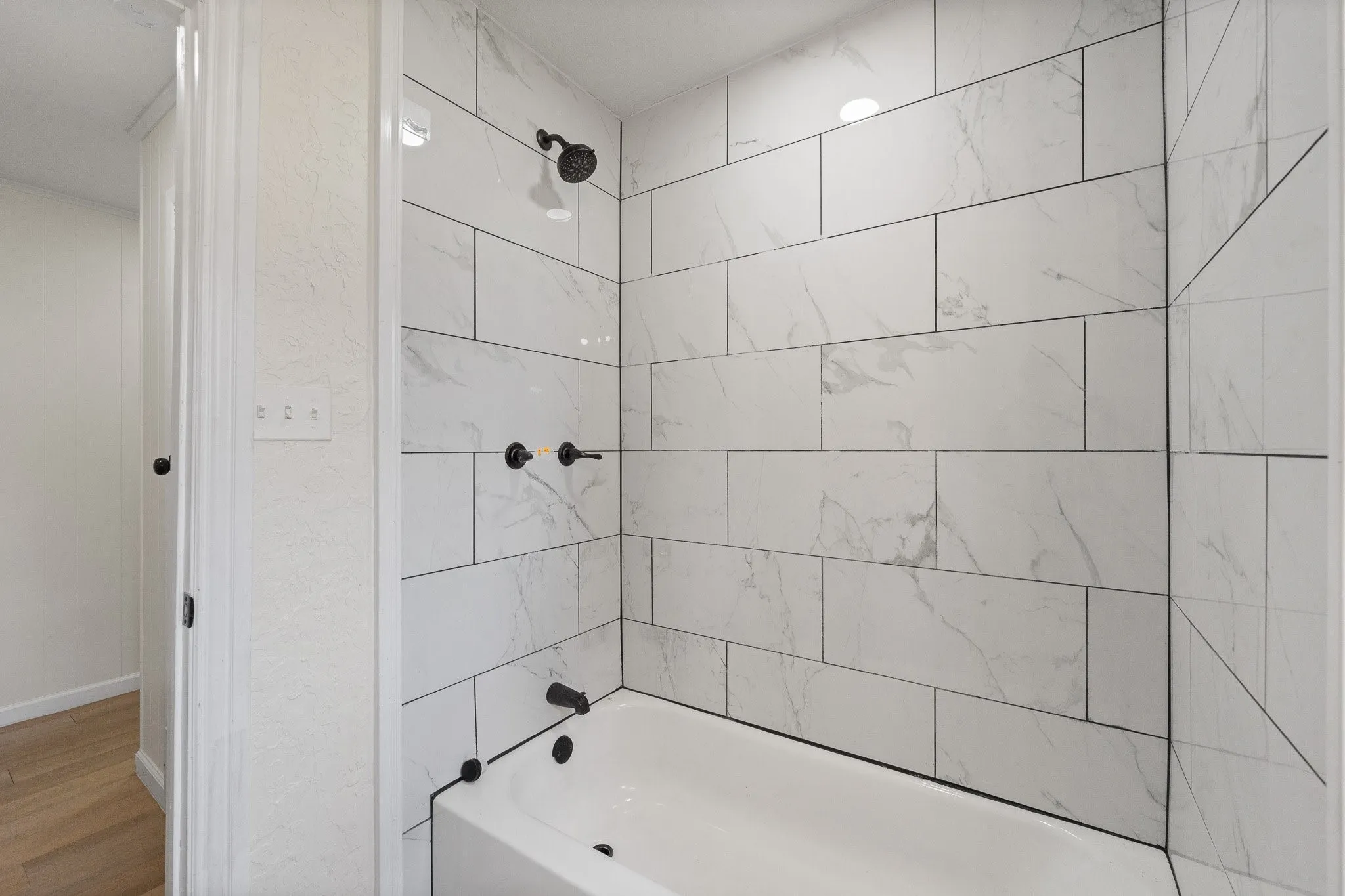 Bathtub and shower combination featuring white subway tile surround with dark grout, matte black showerhead, and matching matte black bath fixtures
