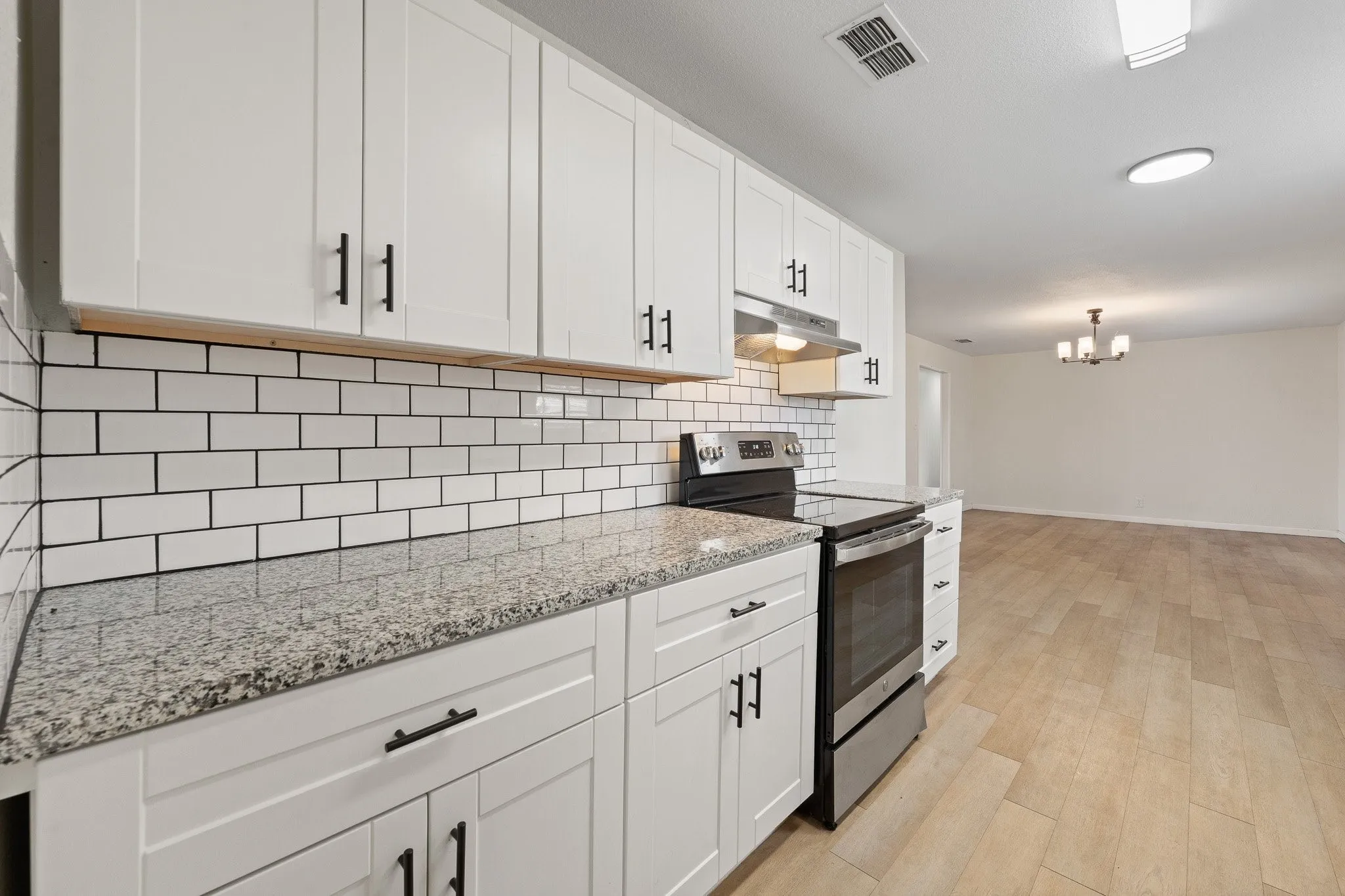 Modern kitchen featuring white shaker cabinetry, granite-style countertops, subway tile backsplash, stainless steel range, and wood-finish flooring