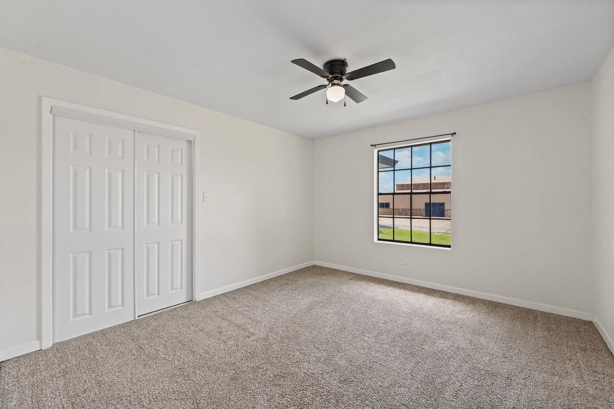 Neutral tone carpeting, a multi-pane window with black trim, and a ceiling fan with integrated lighting