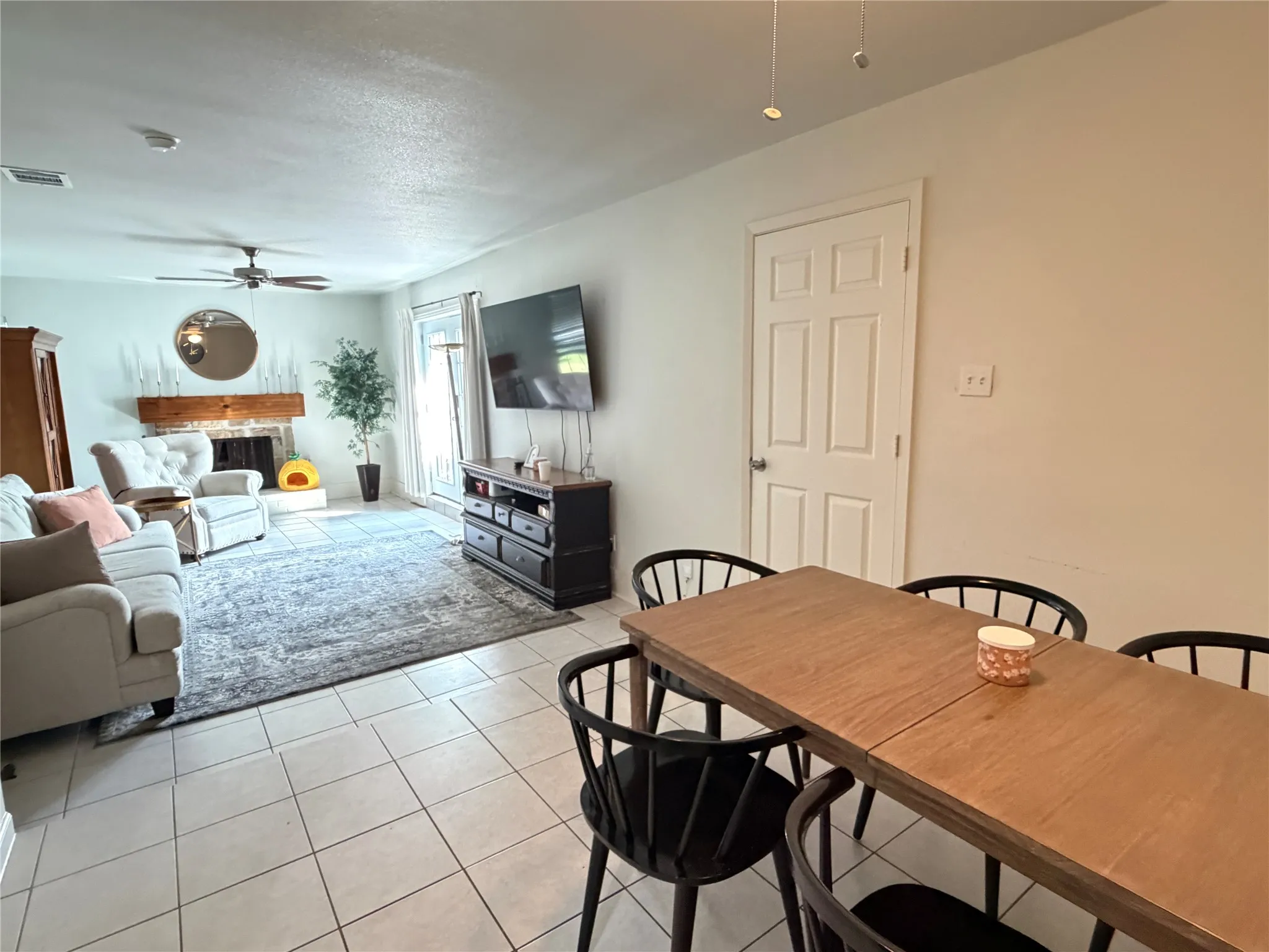 Open-concept living and dining area featuring ceramic tile flooring, a wood-mantel fireplace with a brick surround, and a ceiling fan
