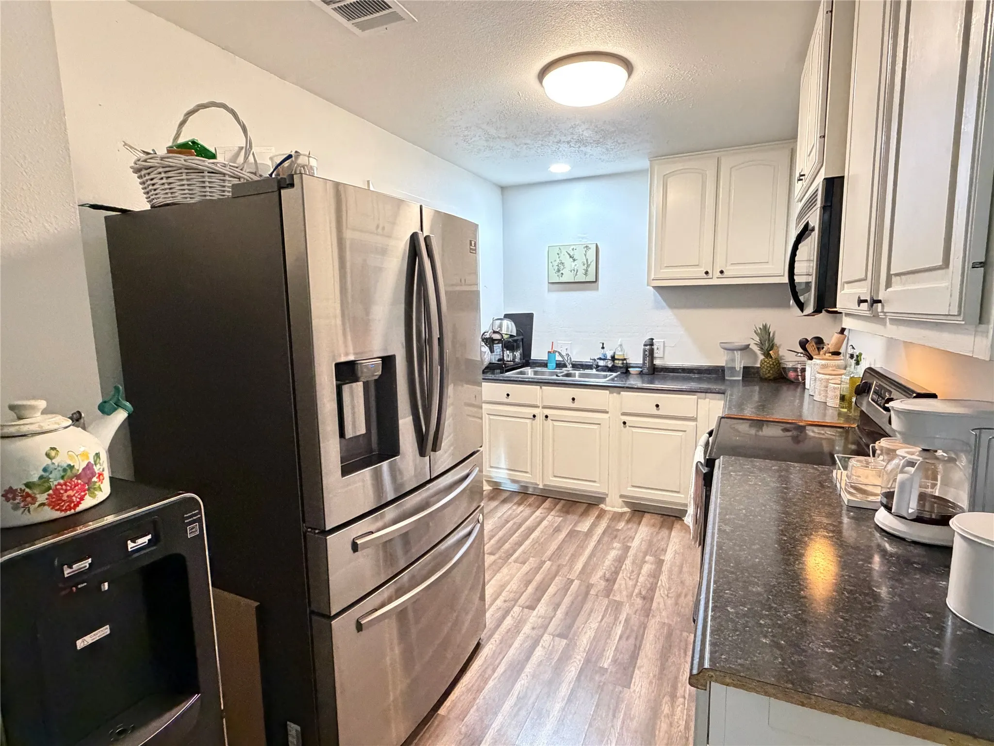 Kitchen featuring a stainless steel French door refrigerator, wood-finish flooring, white cabinetry, dark countertops, and a built-in microwave