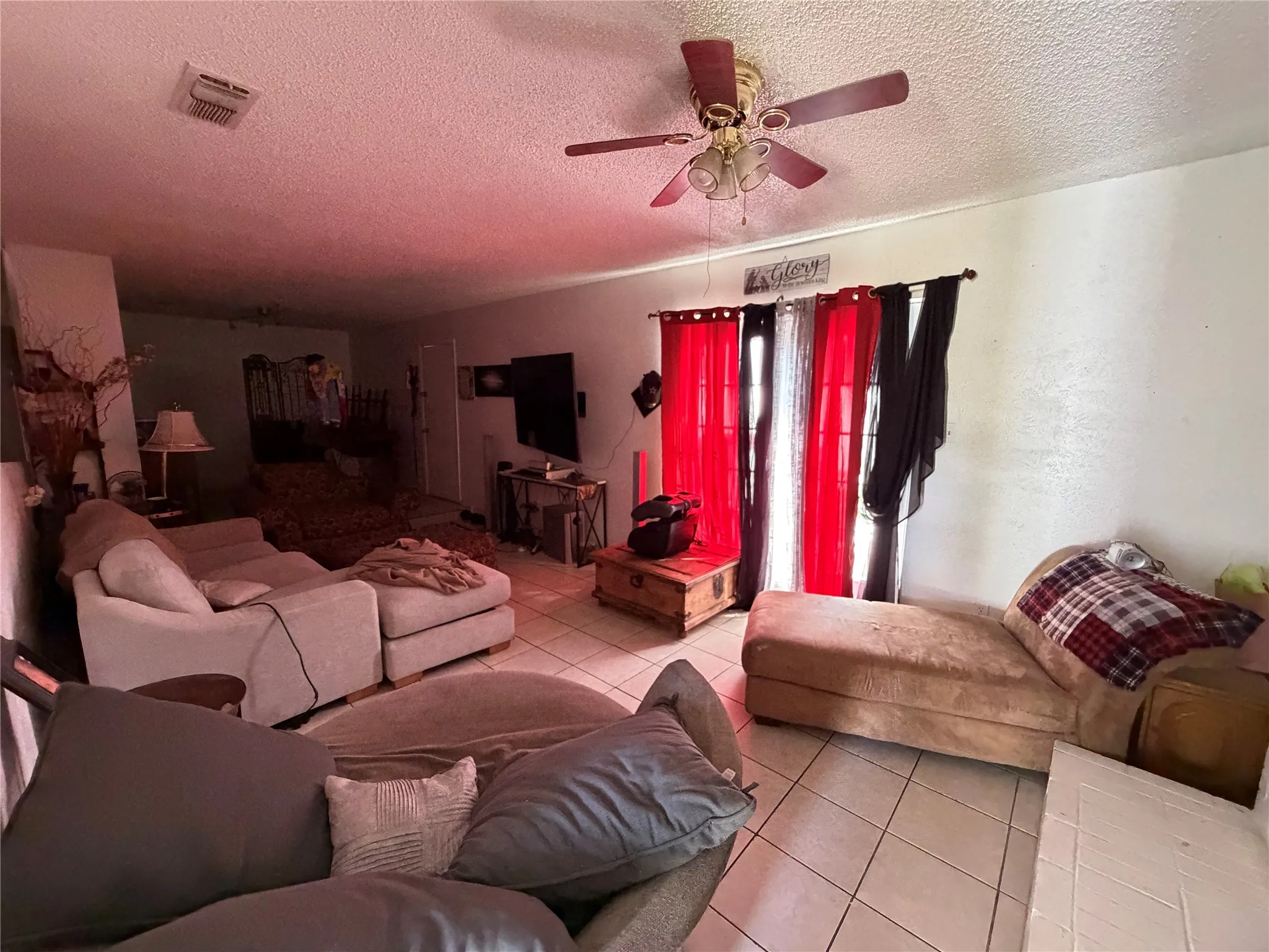 Living area featuring neutral tile flooring, white walls, and a ceiling fan with integrated lighting