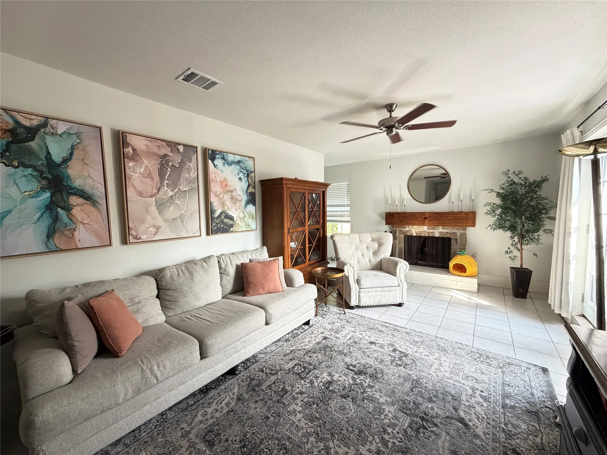 Spacious living area featuring a brick fireplace with a wood mantel, a ceiling fan, and light tile flooring