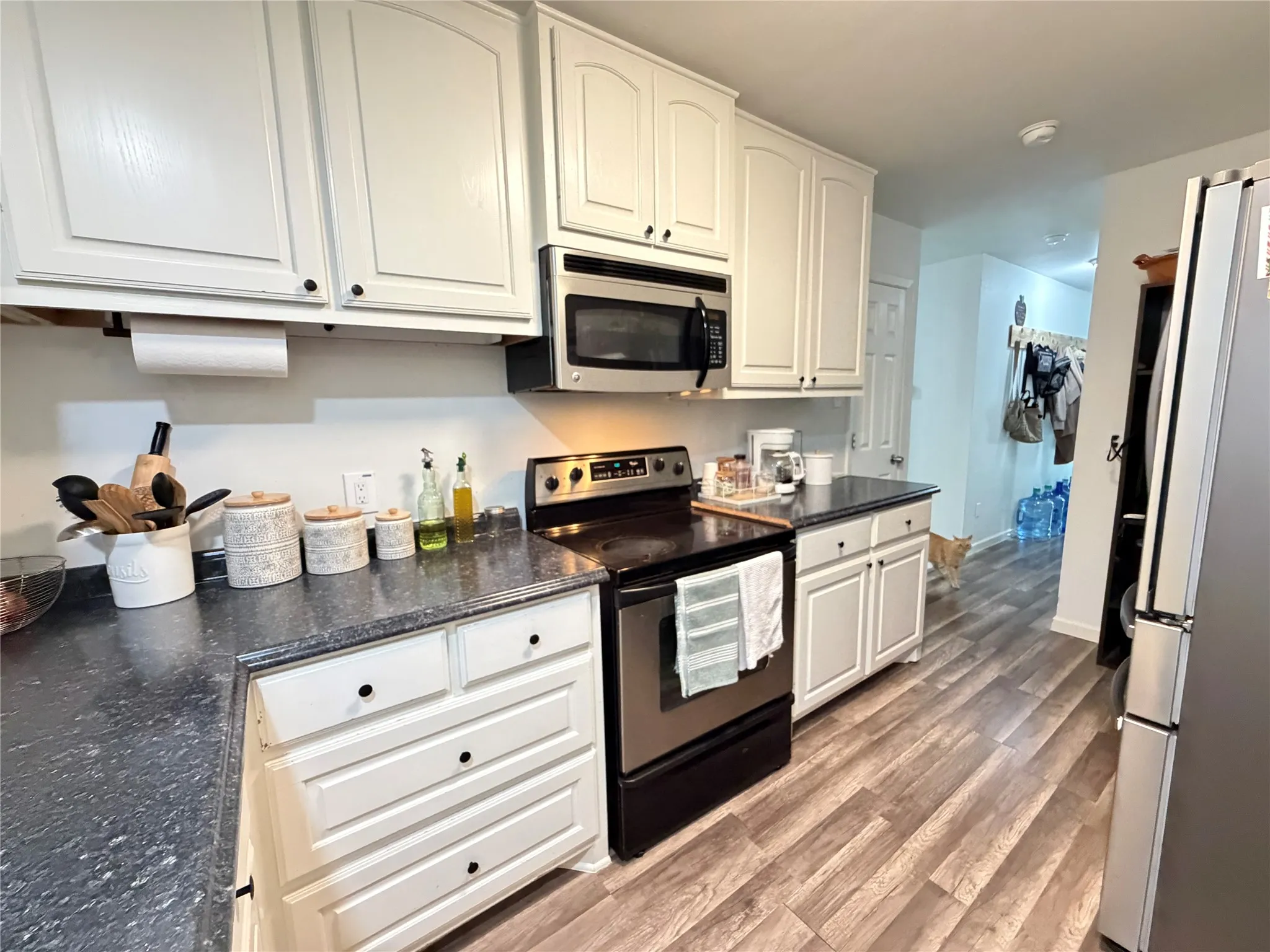 Kitchen featuring white cabinetry with black hardware, dark countertops, stainless steel electric range, and wood-finish flooring