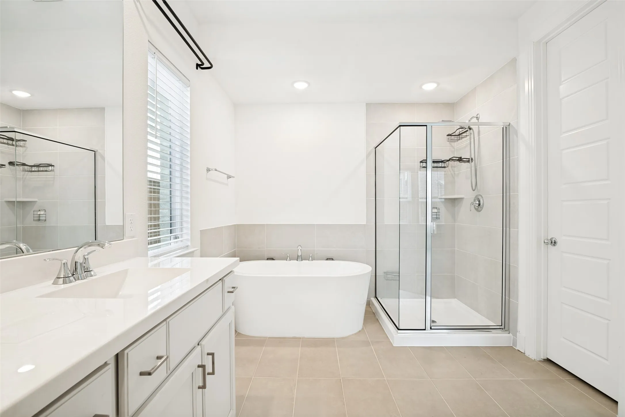 Contemporary bathroom featuring a freestanding soaking tub, glass-enclosed shower, white vanity with integrated sink, and light-toned tile flooring