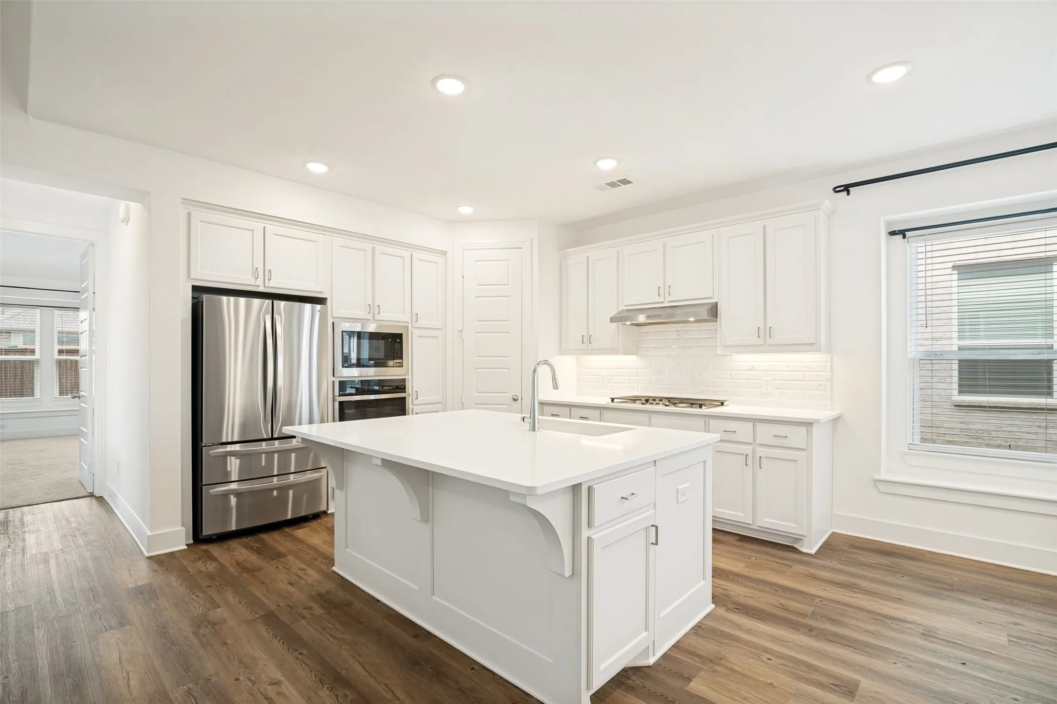 Kitchen featuring a central island with a sink, white cabinetry, stainless steel appliances, wood-finish flooring, and recessed lighting