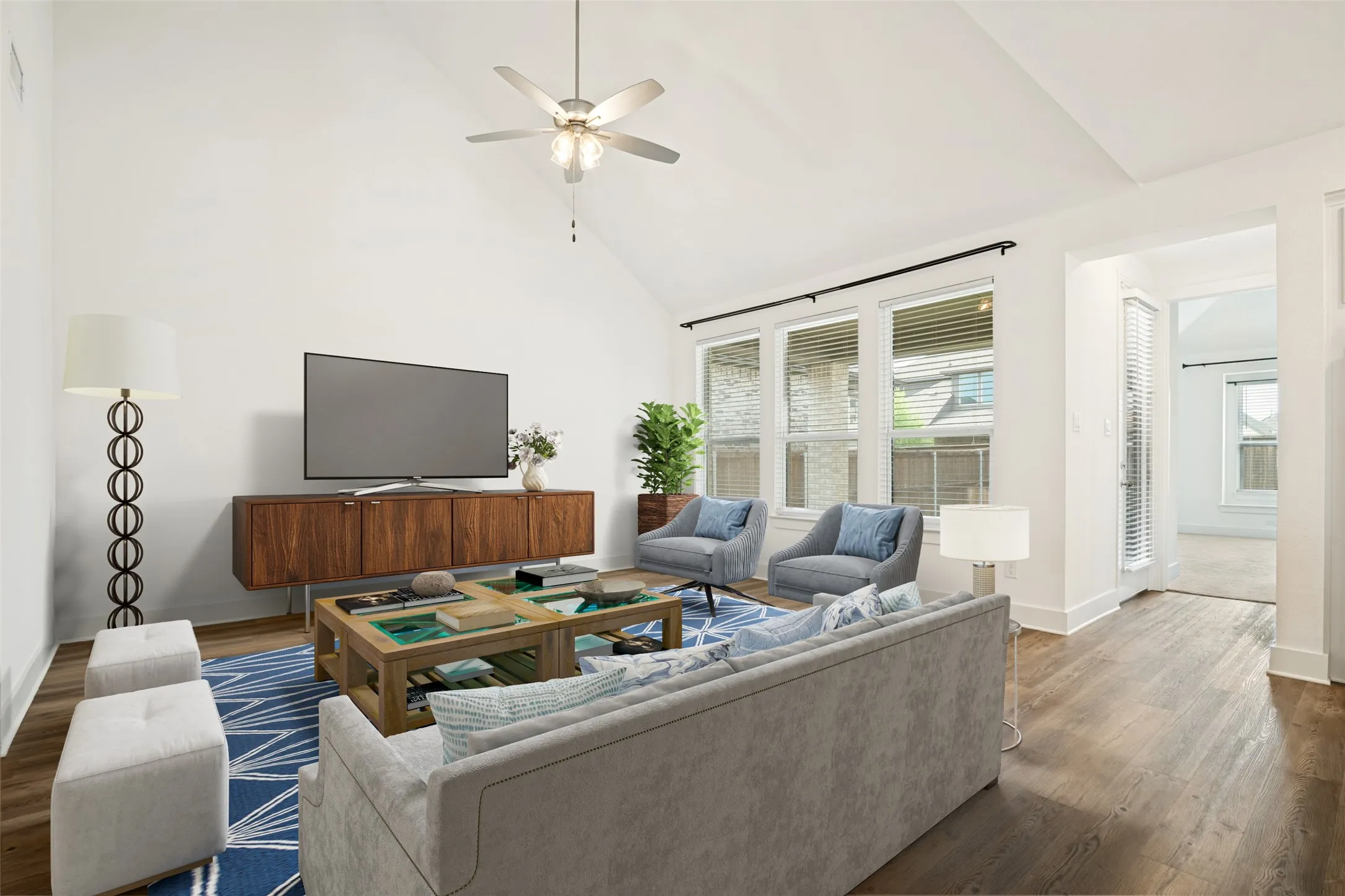 Living area featuring a vaulted ceiling with a ceiling fan, dark wood-finish flooring, and multiple windows with blinds. Digitally staged.