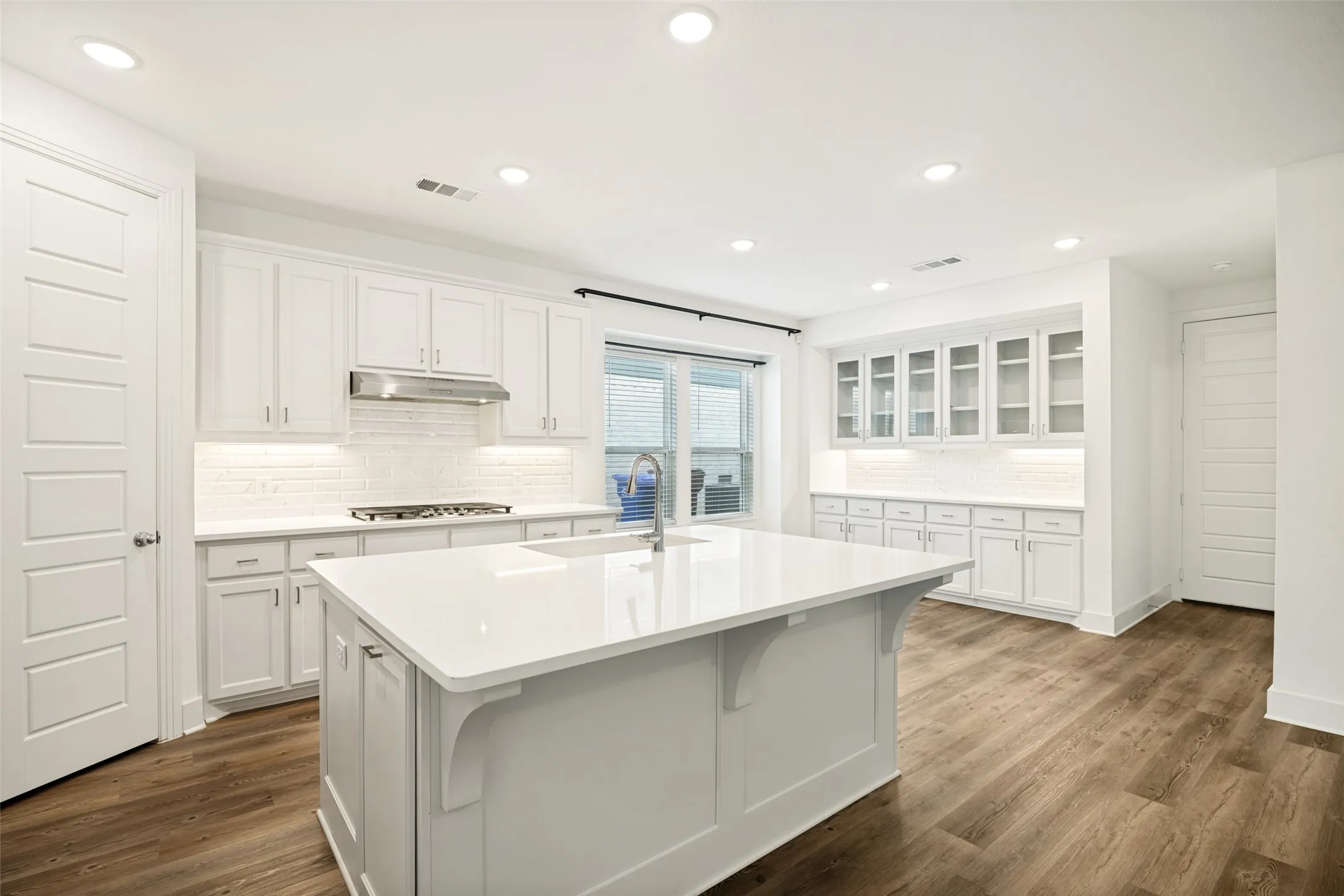 Contemporary kitchen featuring a large central island, white cabinetry, integrated stainless steel appliances, and wood-finish flooring