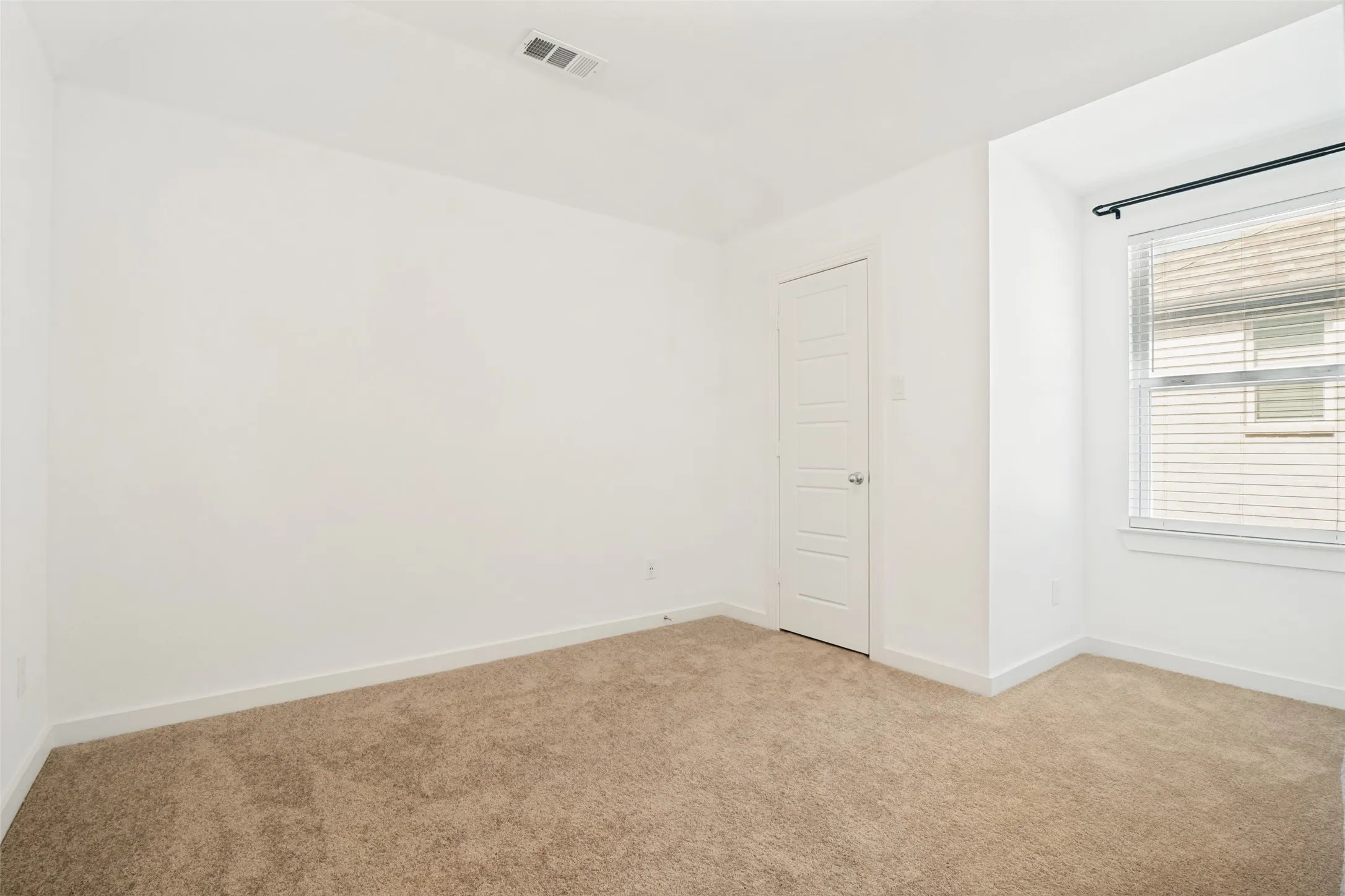 Carpeted room featuring a single window with blinds, a white paneled door, and a ceiling vent