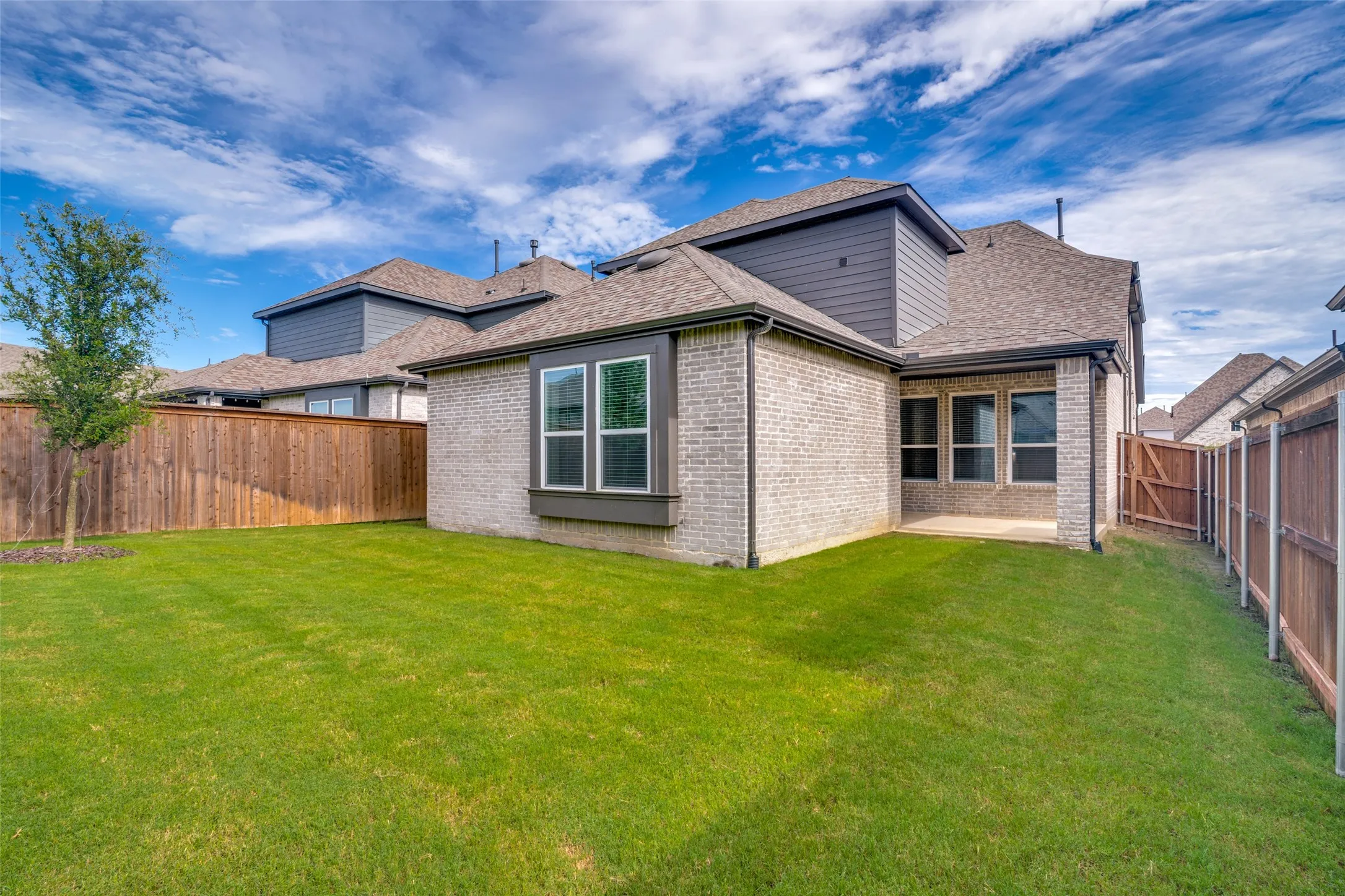 Expansive backyard featuring a manicured lawn, full privacy fencing, and a covered patio