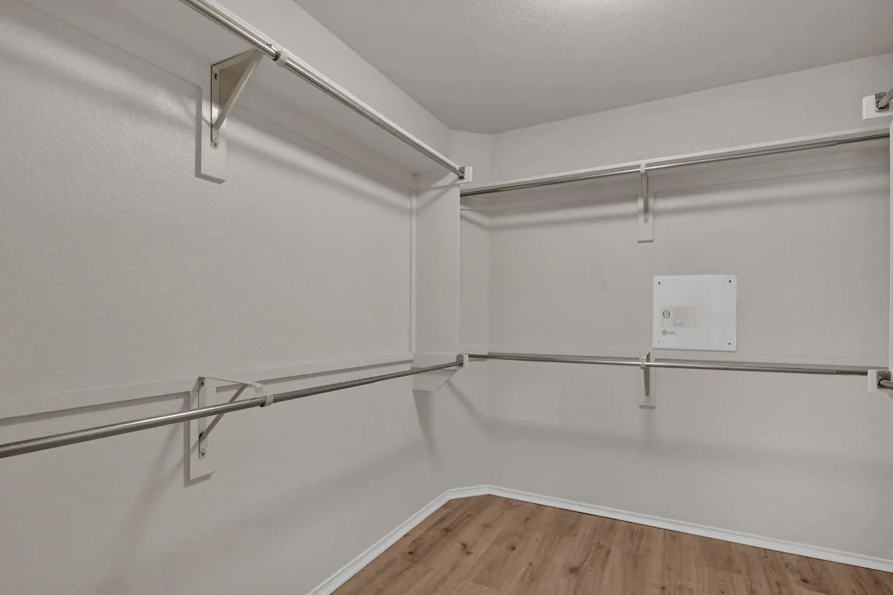 Walk-in closet featuring wood-finish flooring, white walls, and multiple levels of built-in shelving with hanging rods