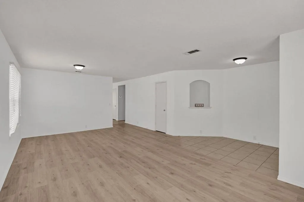 Open-concept living area featuring wood-finish flooring, a distinct tile section, an arched wall niche, a white interior door, and ceiling-mounted light fixtures