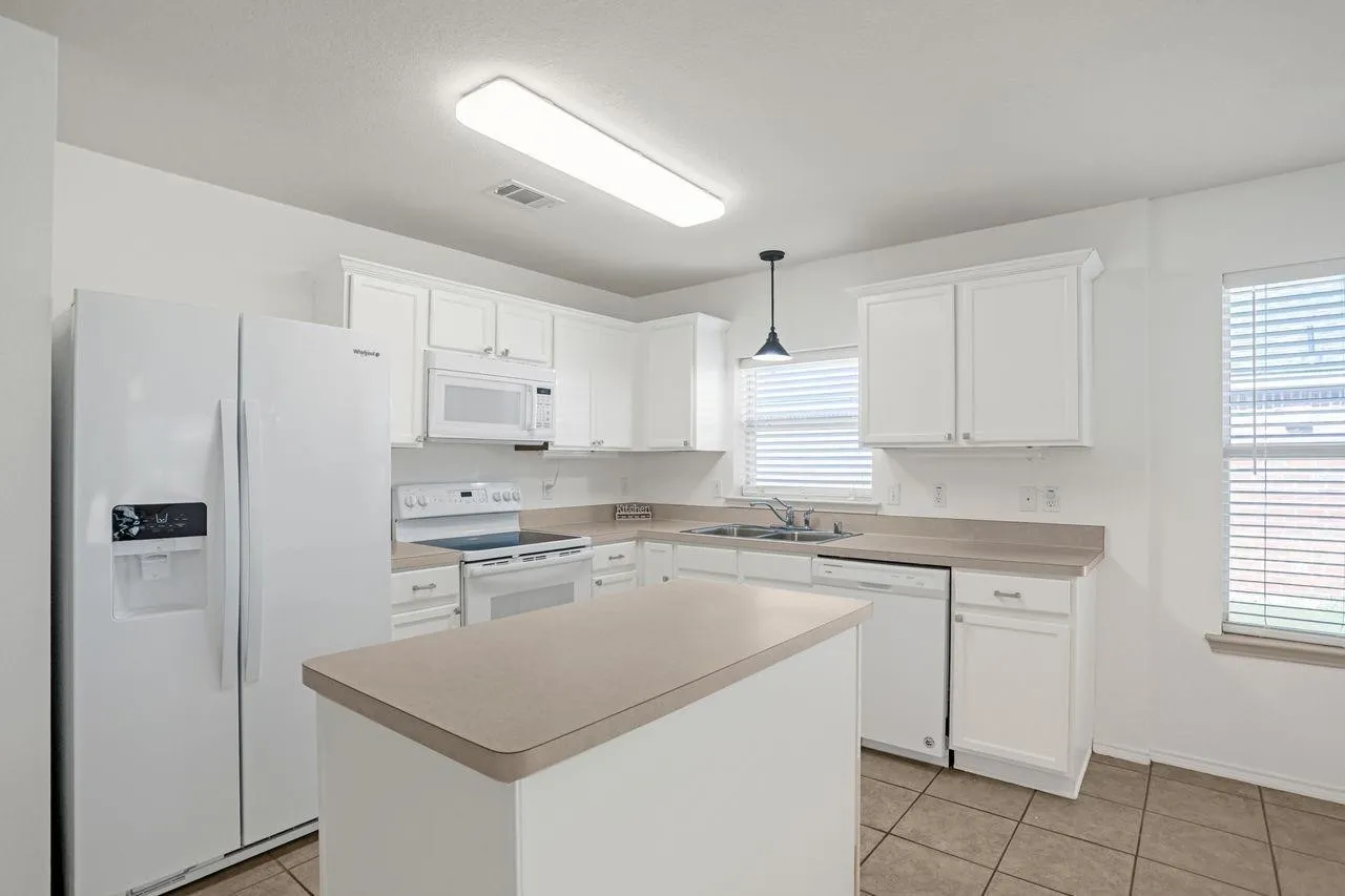 Bright kitchen with white cabinetry and appliances, featuring a central island with a solid surface countertop