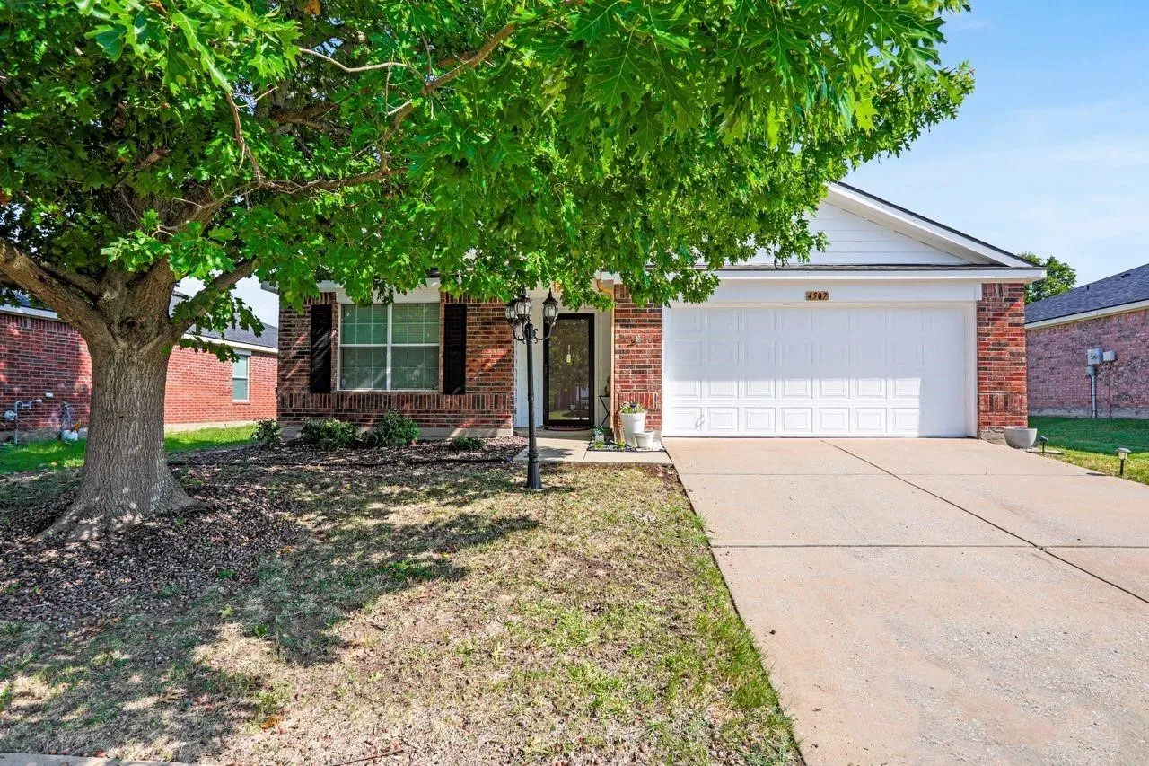 Brick facade residence featuring a two-car garage, concrete driveway, and a mature shade tree
