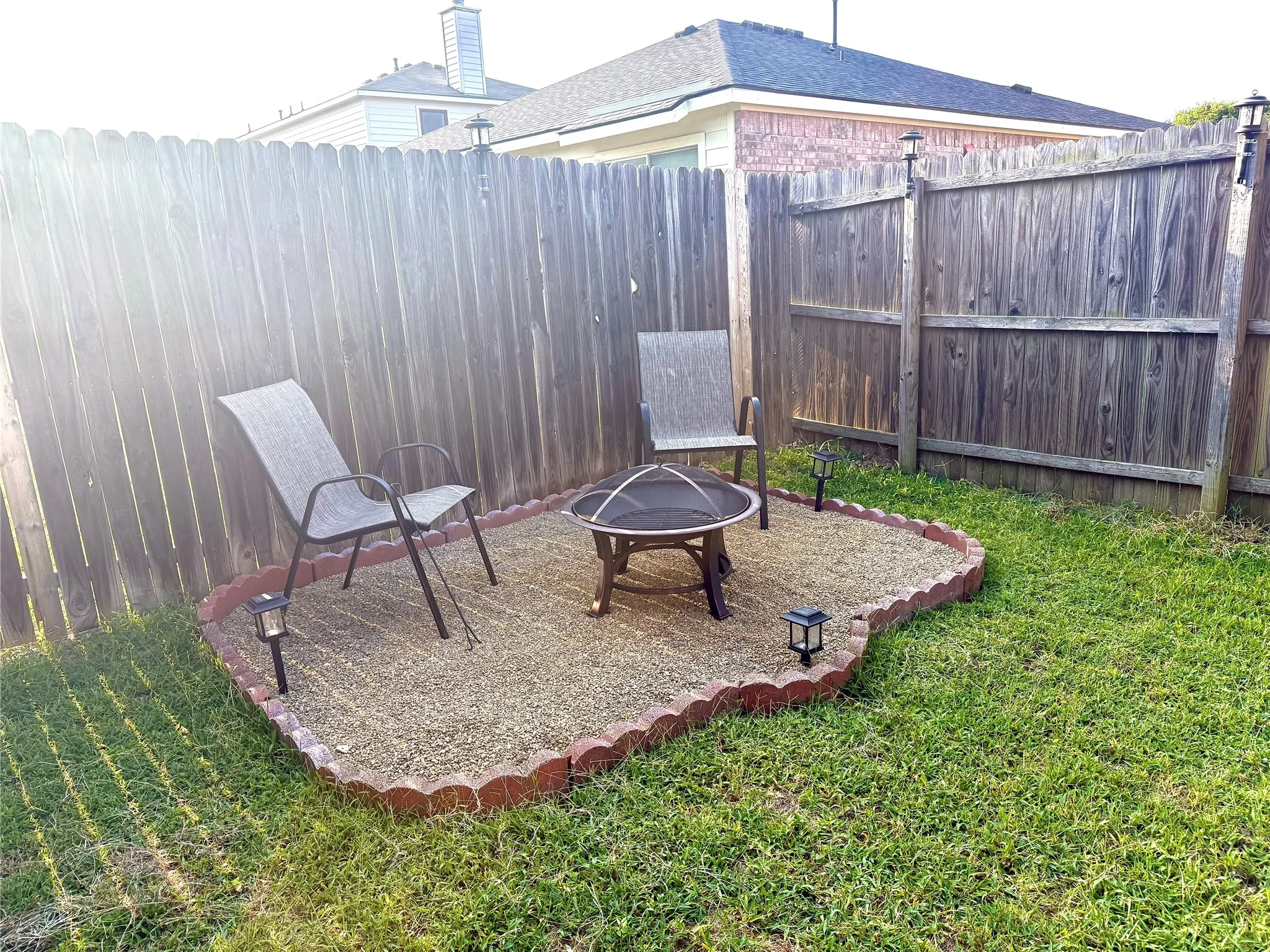 Backyard seating area featuring a pea gravel foundation, decorative brick edging, a privacy fence, and integrated solar lighting
