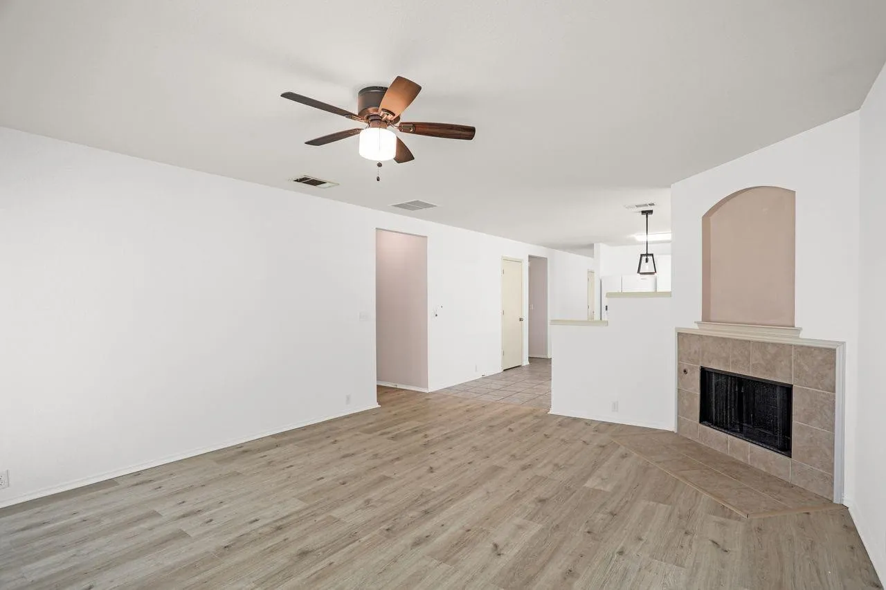 Spacious living area featuring wood-finish flooring, a ceiling fan with integrated lighting, and a tiled corner fireplace