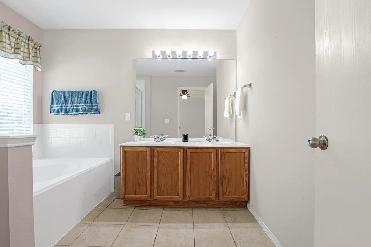 Bathroom featuring a wood-finish vanity with dual sinks, a large mirror, and a wall-mounted light fixture
