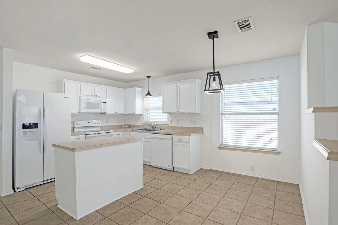 Kitchen featuring white cabinetry, light countertops, an island, tile flooring, and a large window with blinds