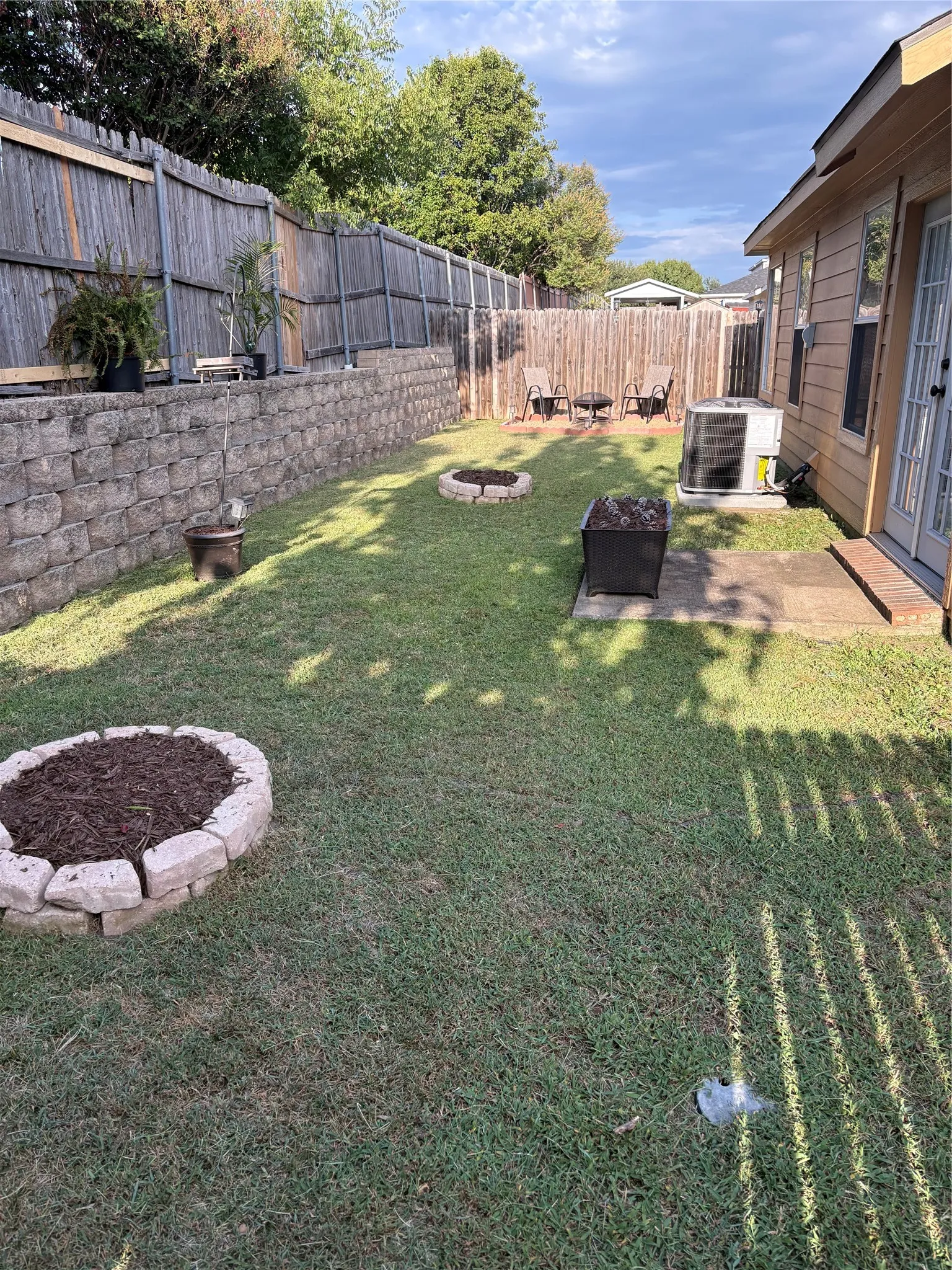 Expansive backyard featuring a retaining wall with integrated landscaping, a privacy fence, and a patio area