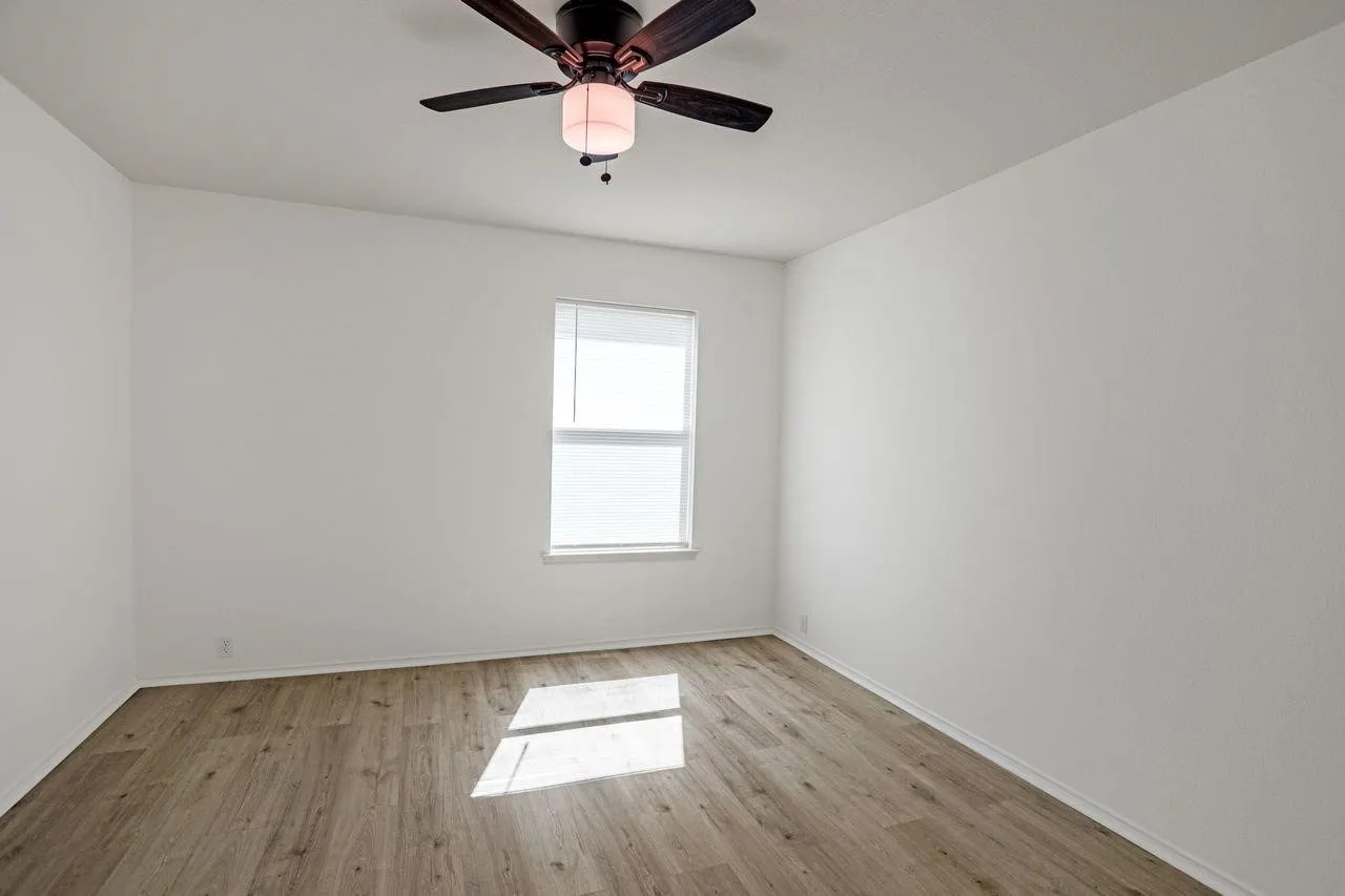 Room featuring wood-finish flooring, a ceiling fan with integrated lighting, a window with blinds, white walls, and white baseboards