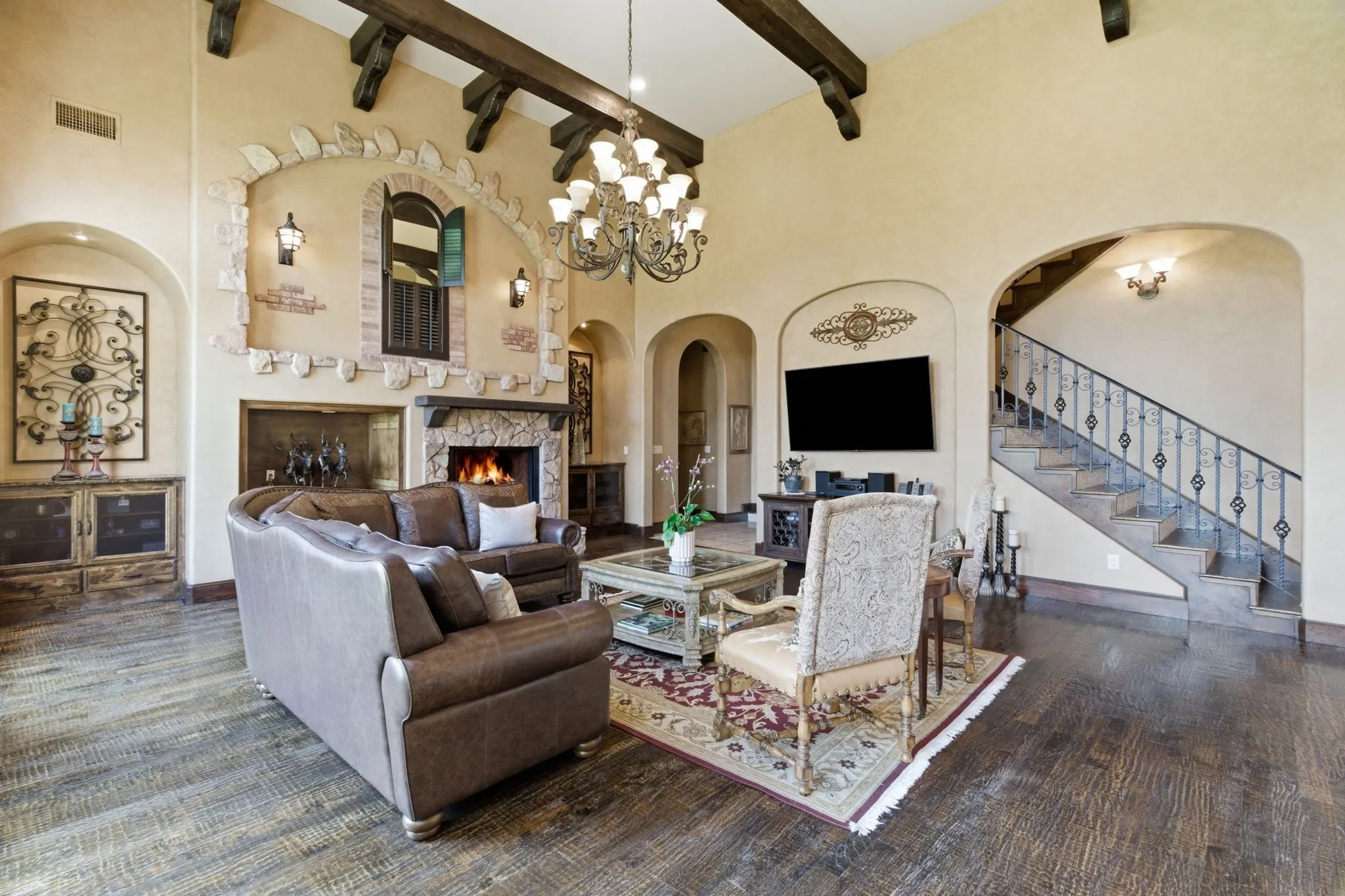 Spacious living area featuring exposed ceiling beams, a stone-clad fireplace, and wood-finish flooring