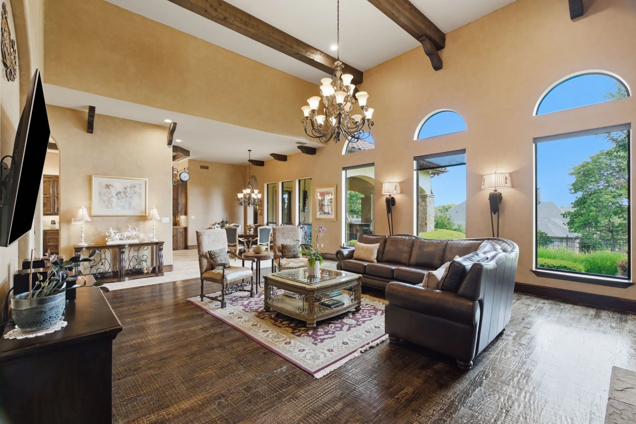 Vaulted ceiling with exposed wood beams, expansive windows, wood-finish flooring, and a chandelier lighting fixture