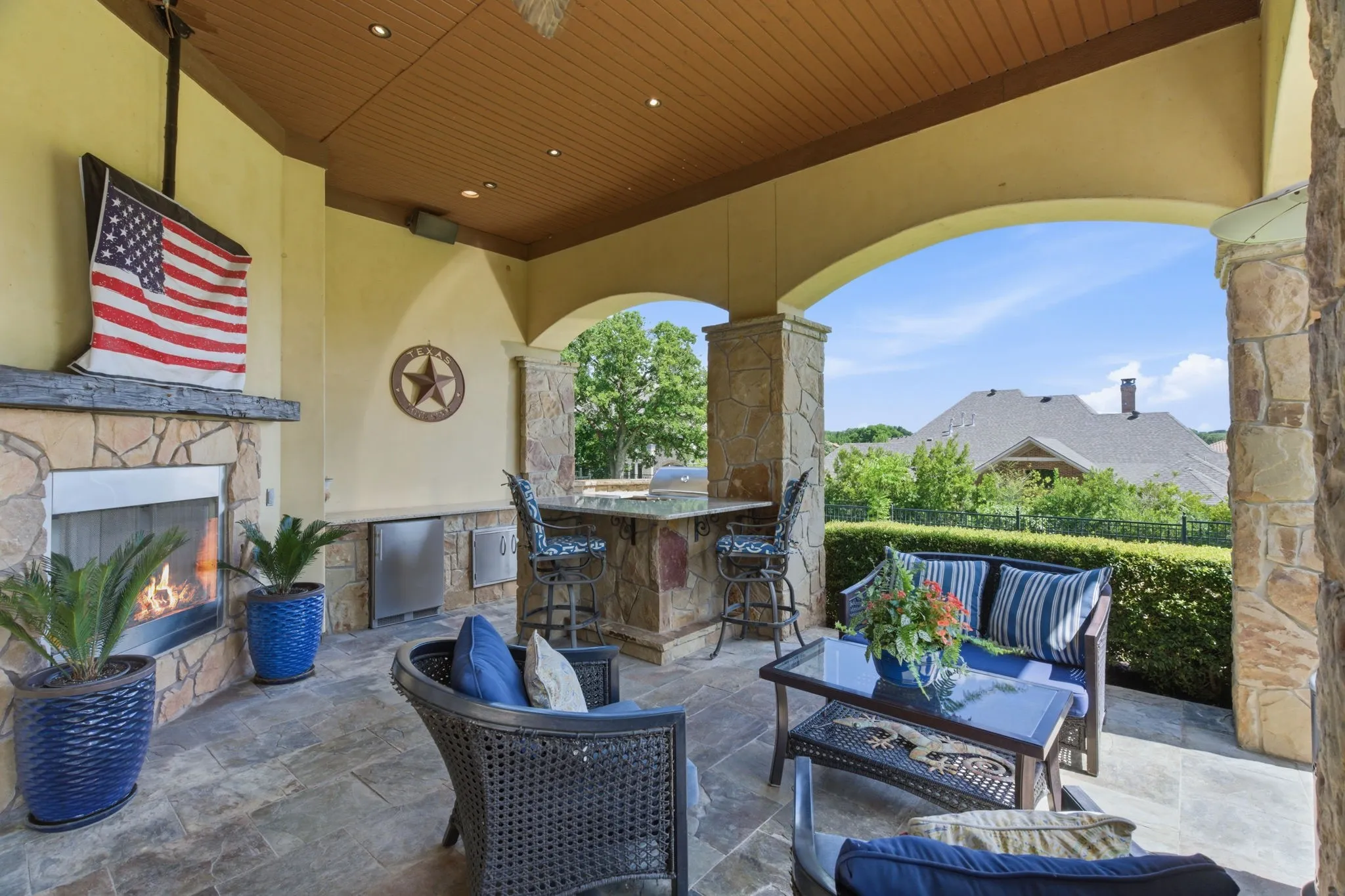 Covered patio featuring an outdoor stone fireplace, built-in outdoor kitchen with stainless steel appliances, stone slab countertop, stone columns, and stone flooring