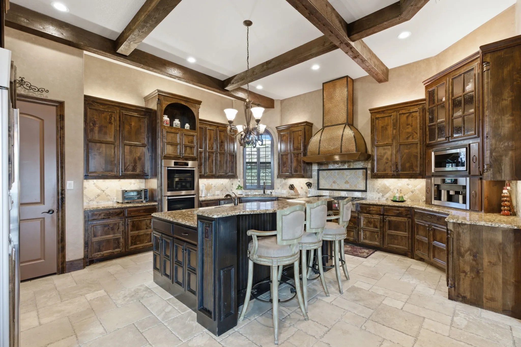 Gourmet kitchen with exposed wood beams, custom wood cabinetry, stone countertops, and a large central island with integrated seating