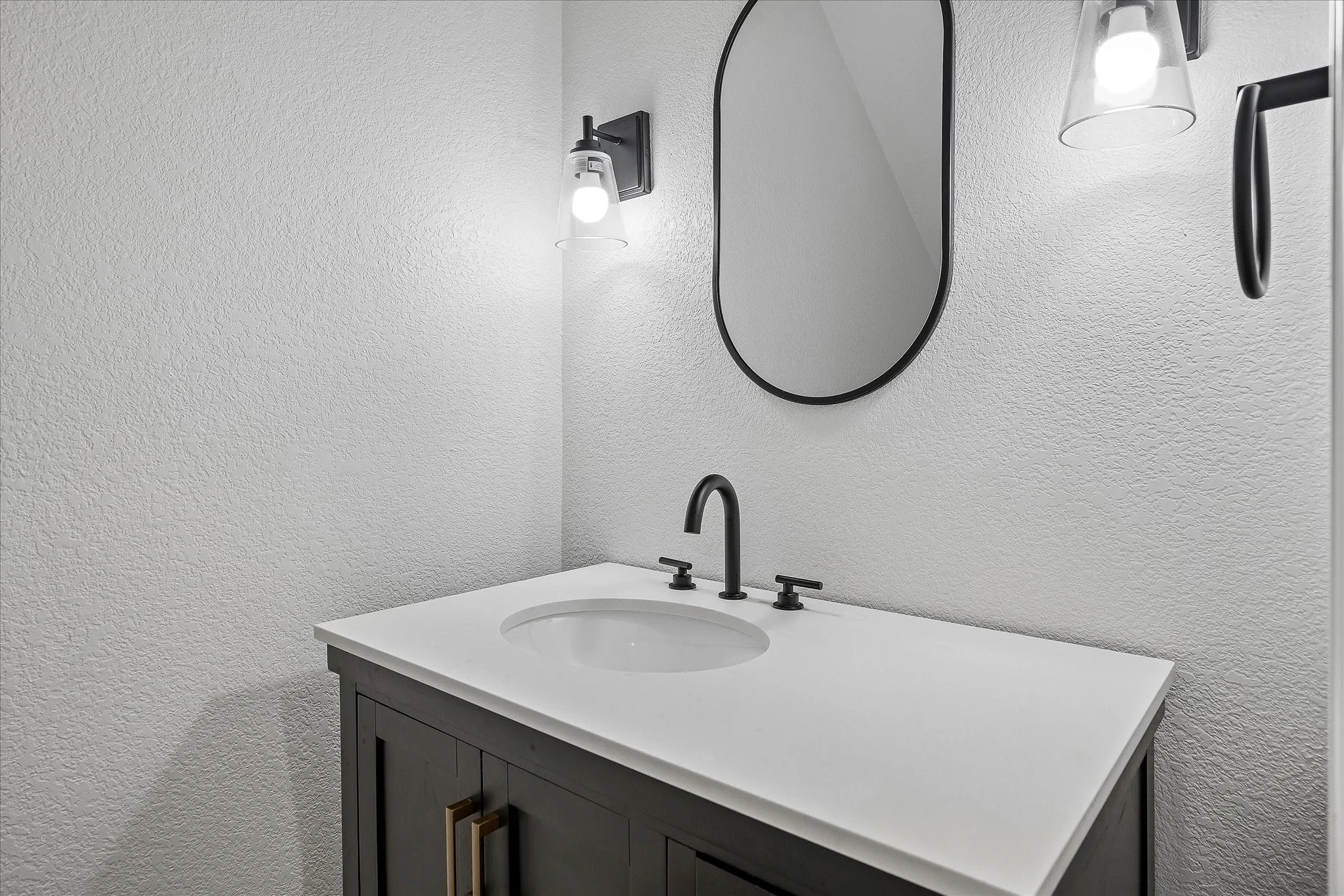 Vanity featuring a dark wood-finish cabinet, white countertop with an integrated sink, matte black faucet, and an oval mirror with a black frame