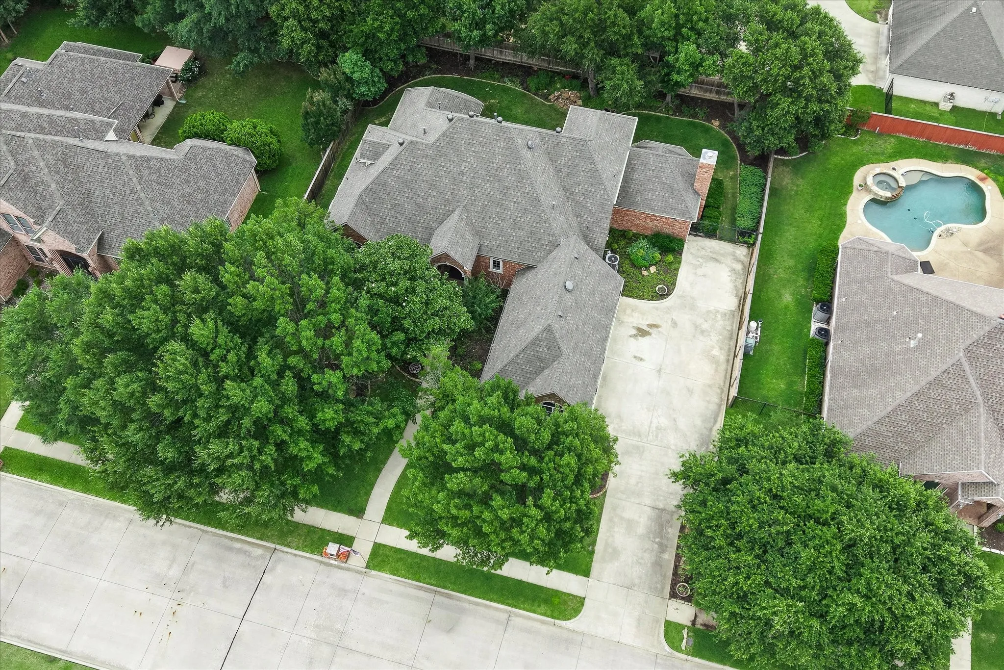 Spacious corner property featuring a multi-gabled roofline, brick exterior, concrete driveway, and mature landscaping